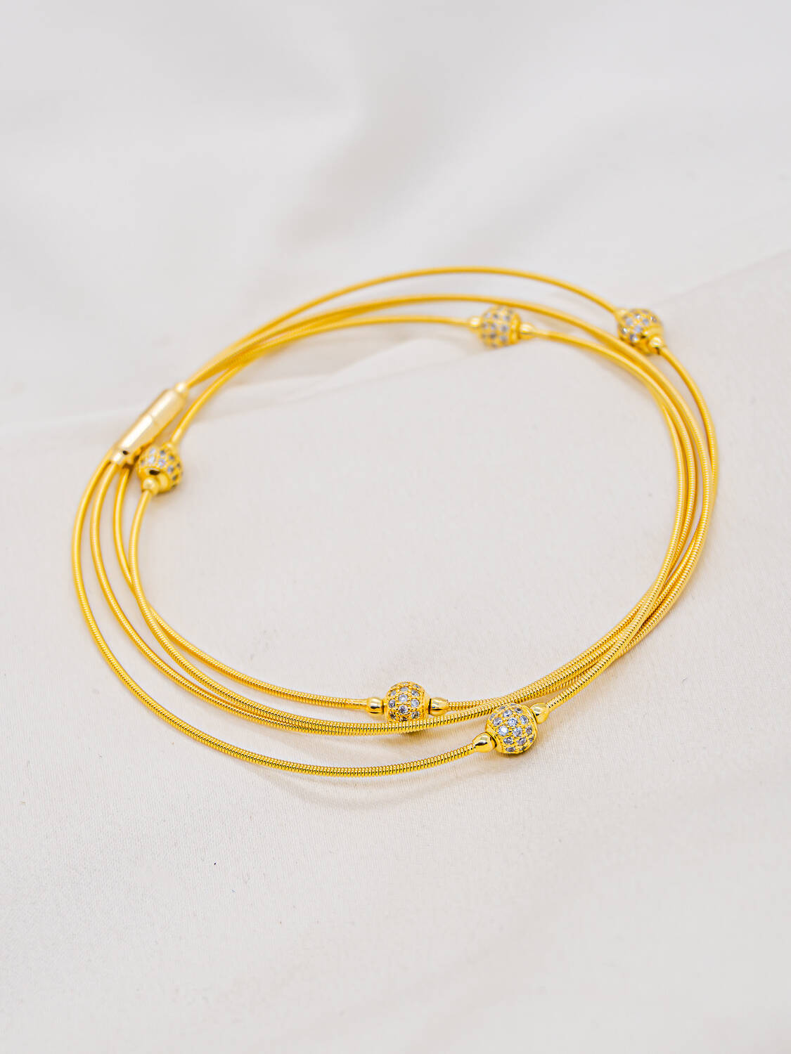 Bracelet doré aux fils fins enroulés, parsemé de petites boules serties de pierres claires