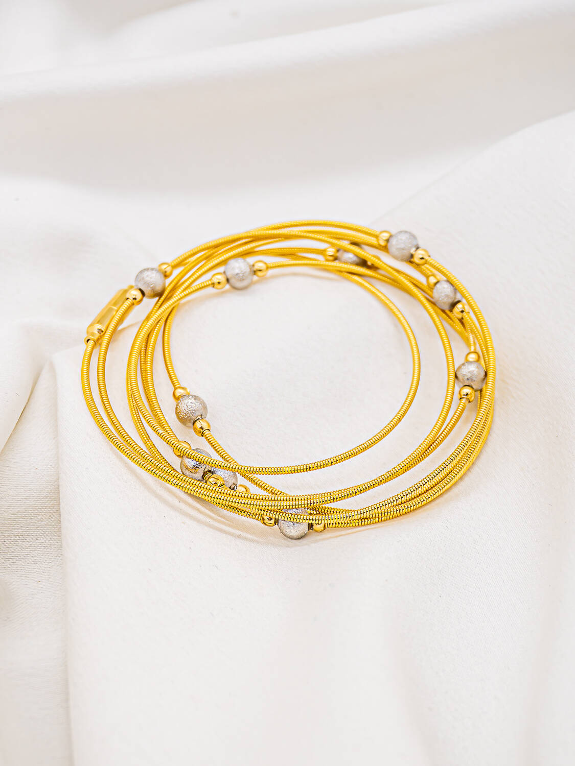 Bracelet à plusieurs tours de fils dorés et boules argentées grainées, posé sur tissu