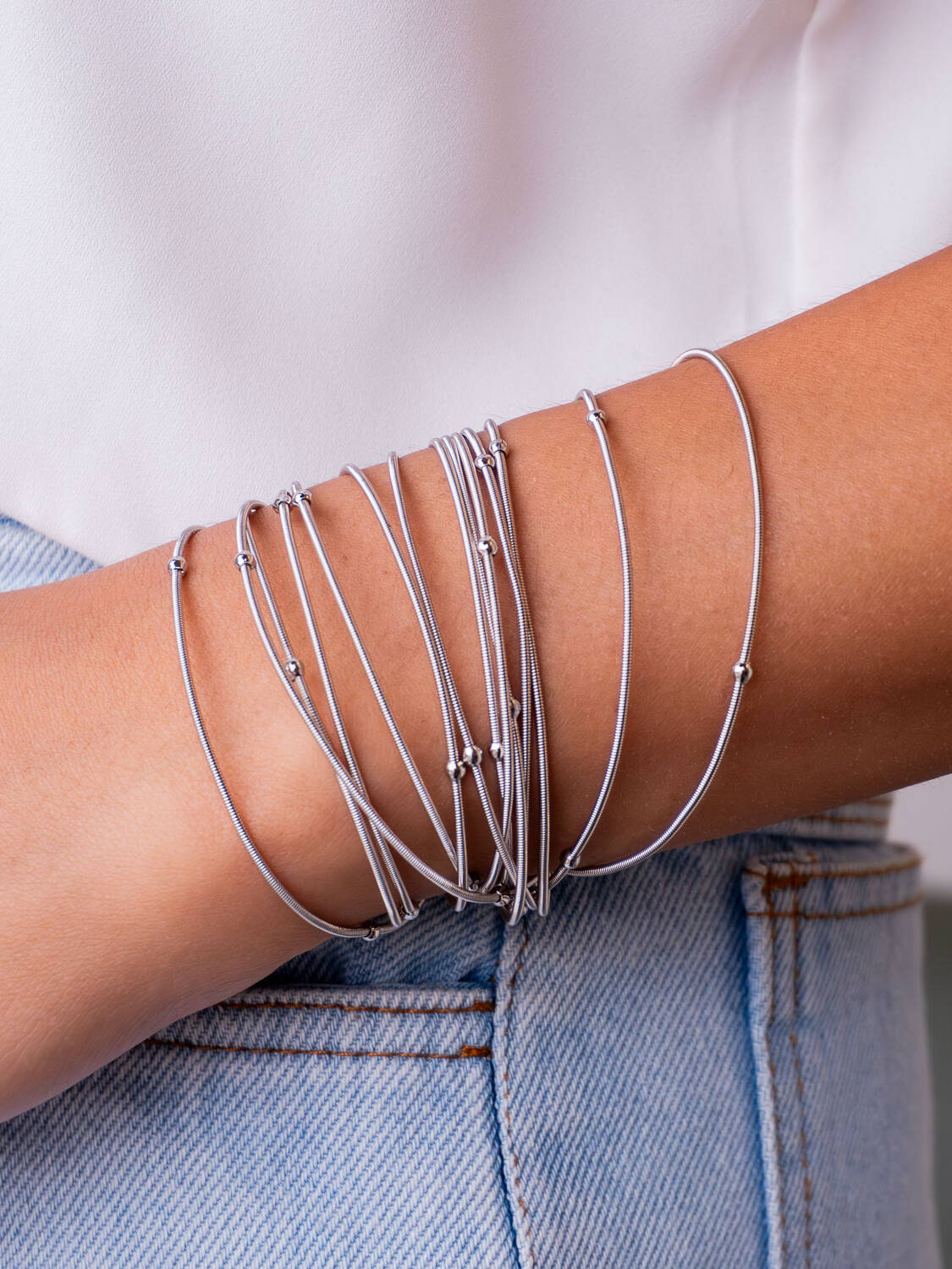 Bracelet argenté à plusieurs tours de fils fins avec petites boules, porté sur un jean