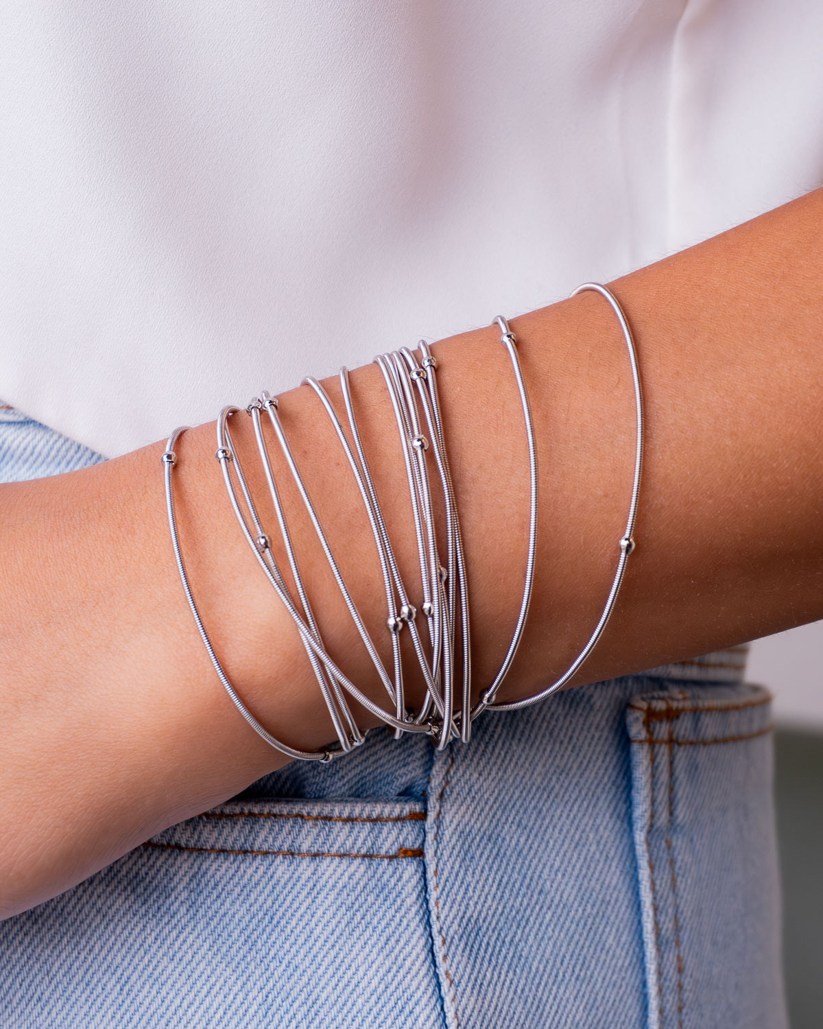 Pulseira prateada de várias voltas de fios finos com bolinhas, usada com jeans