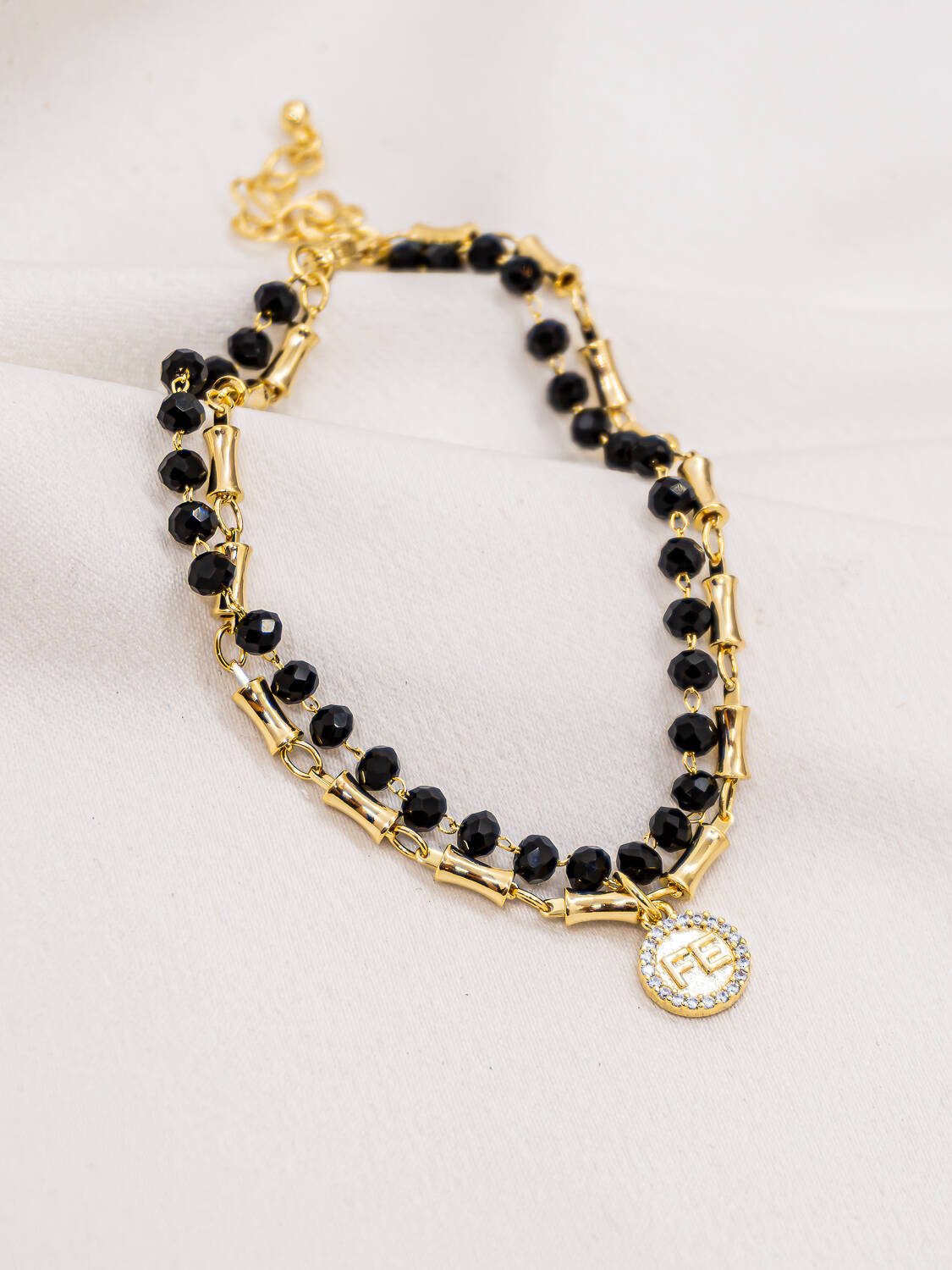 Bracelet doré à deux rangs, cristaux noirs facettés et médaille ronde ornée de pierres claires