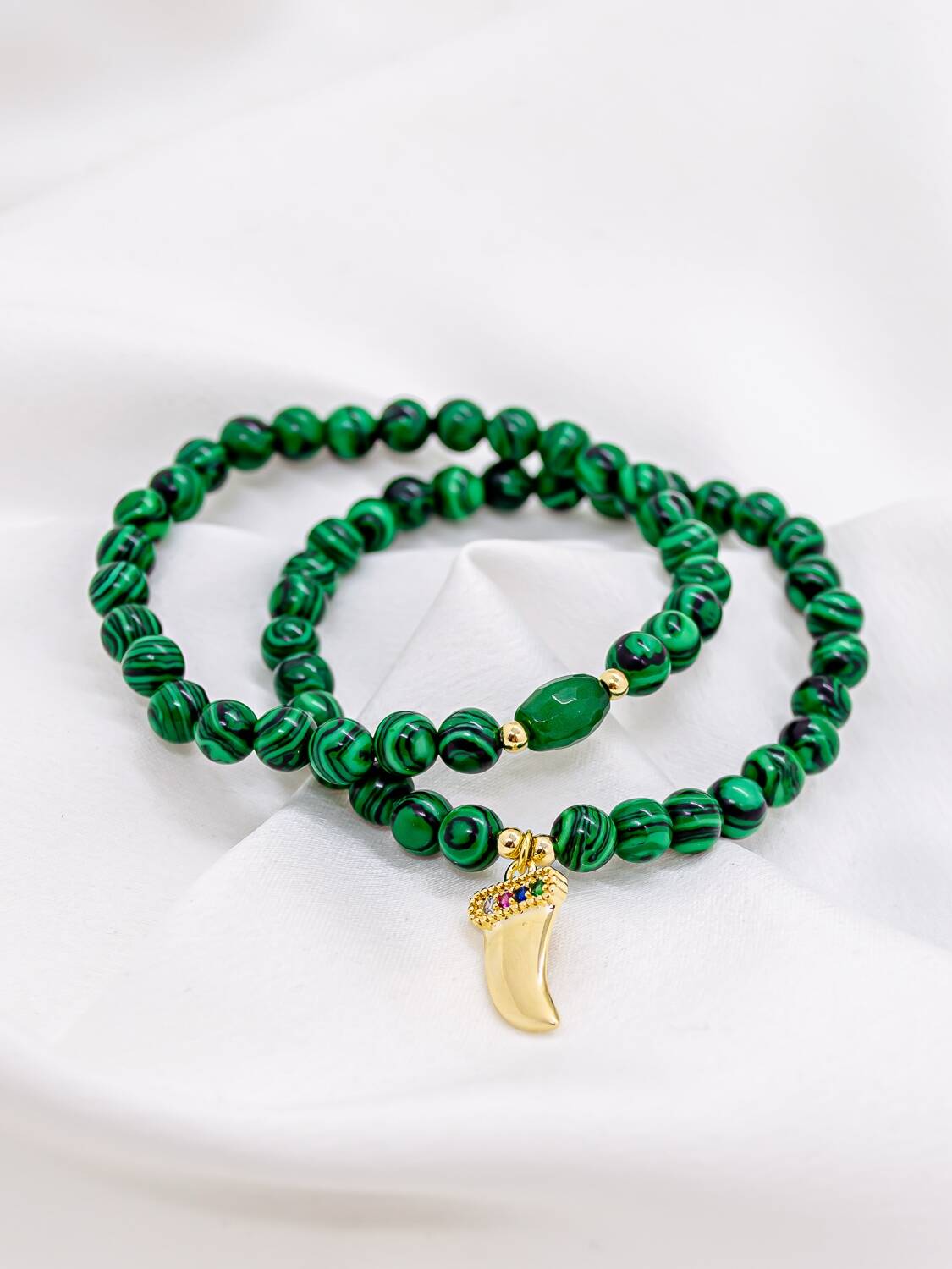 Deux bracelets de perles vertes veinées, l’un avec pendentif doré en forme de dent