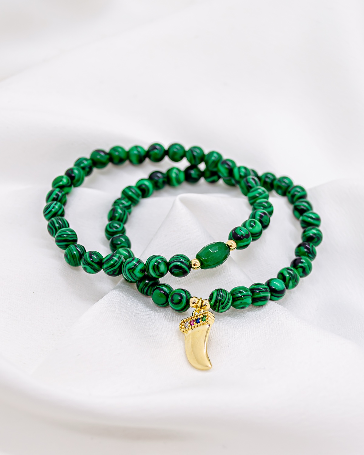 Duas pulseiras de contas verdes com veios, uma com pingente dourado em forma de dente