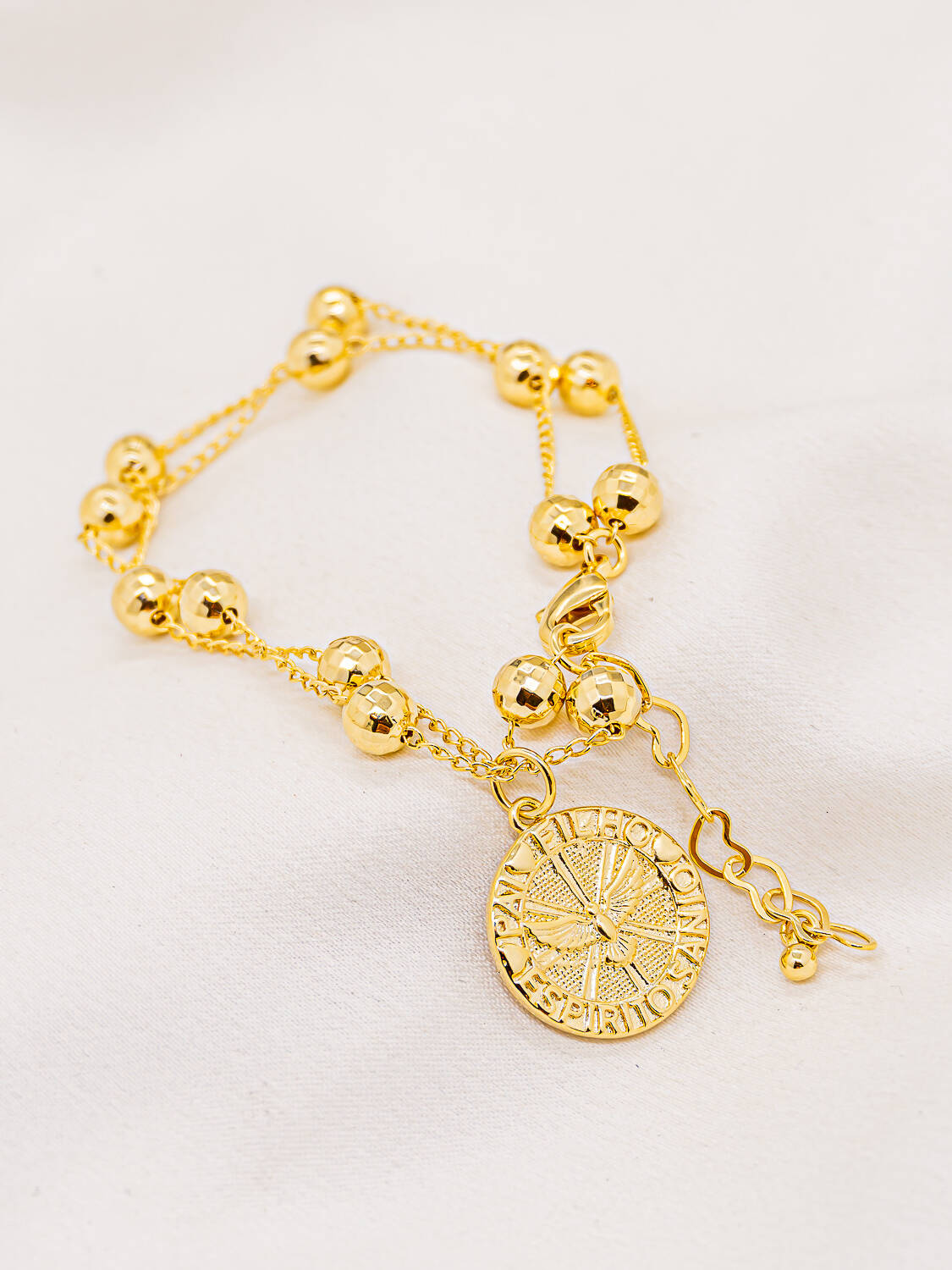 Bracelet doré à double chaîne, boules à facettes et médaille ronde gravée d’une colombe