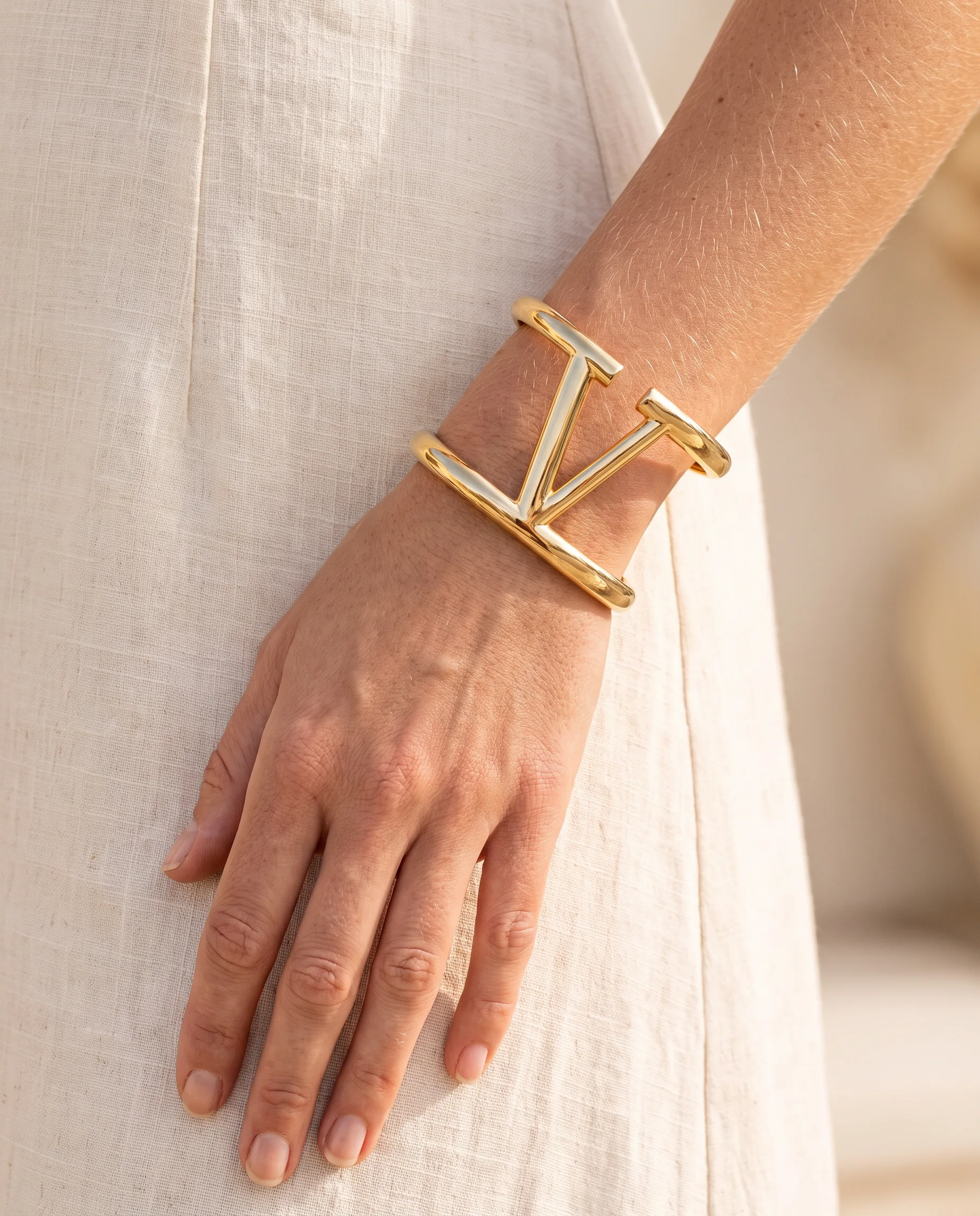 Gold V openwork cuff worn on wrist, over a linen dress