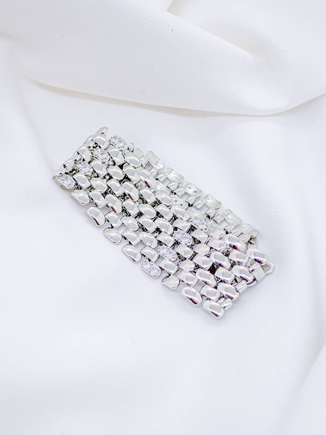 Large bracelet argenté en maillons plats polis, avec quelques pierres claires, sur tissu blanc