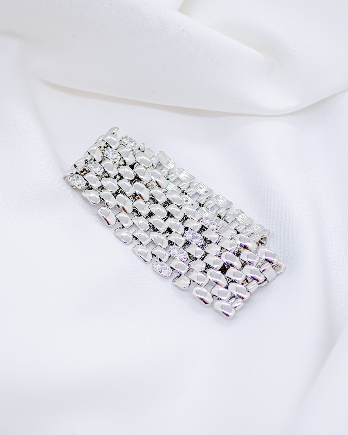 Large bracelet argenté en maillons plats polis, avec quelques pierres claires, sur tissu blanc