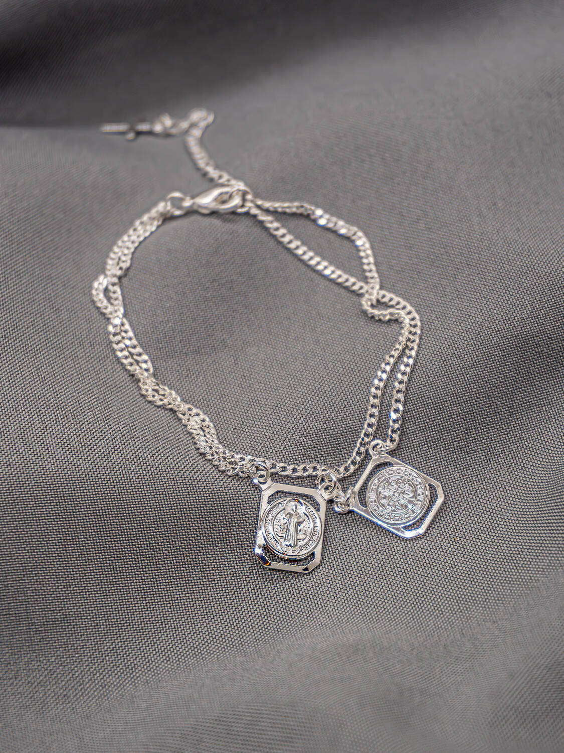 Bracelet argenté à double chaîne gourmette avec deux petites plaques gravées, sur tissu gris
