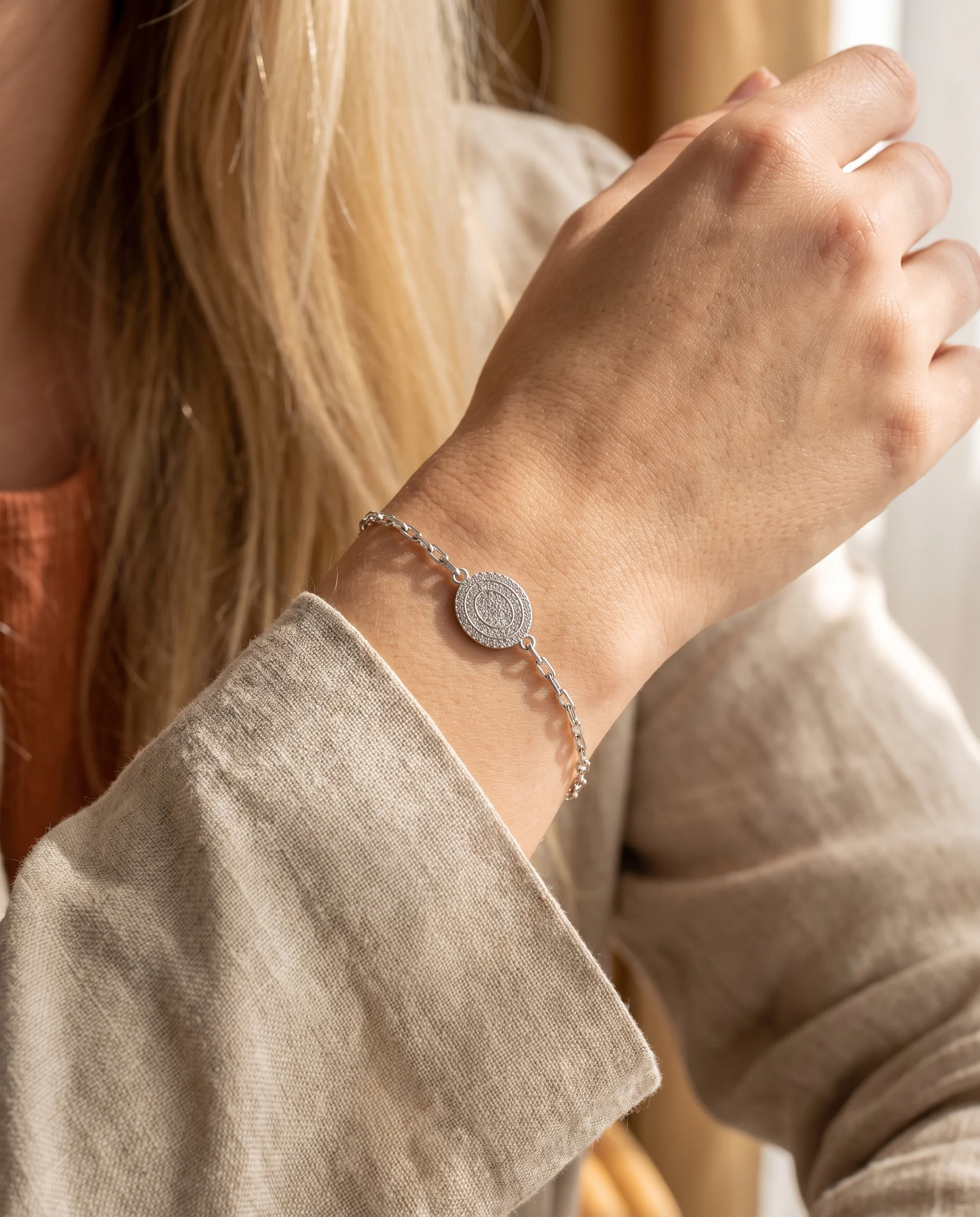 Pulseira de elos ovais, pingente oval cravejado acabamento prateado, usada no pulso, vista de perto