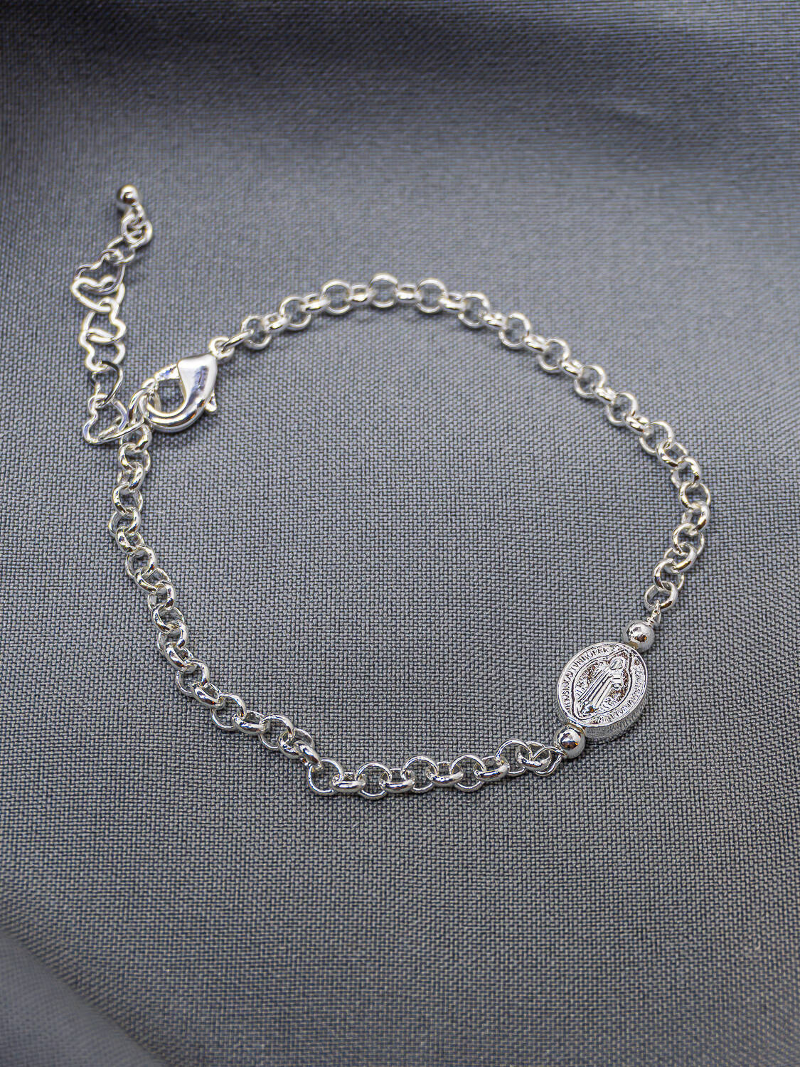 Bracelet argenté à petits maillons ronds avec médaille ovale de Saint Benoît, sur tissu gris