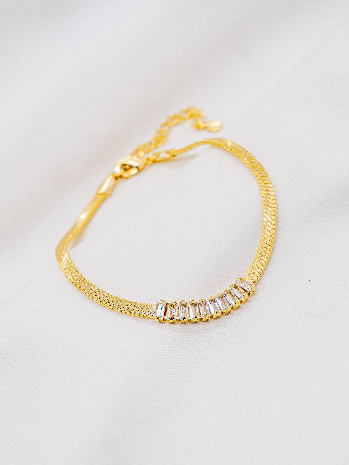 Bracelet doré en chaîne plate texturée avec rangée centrale de petites pierres claires rectangulaires