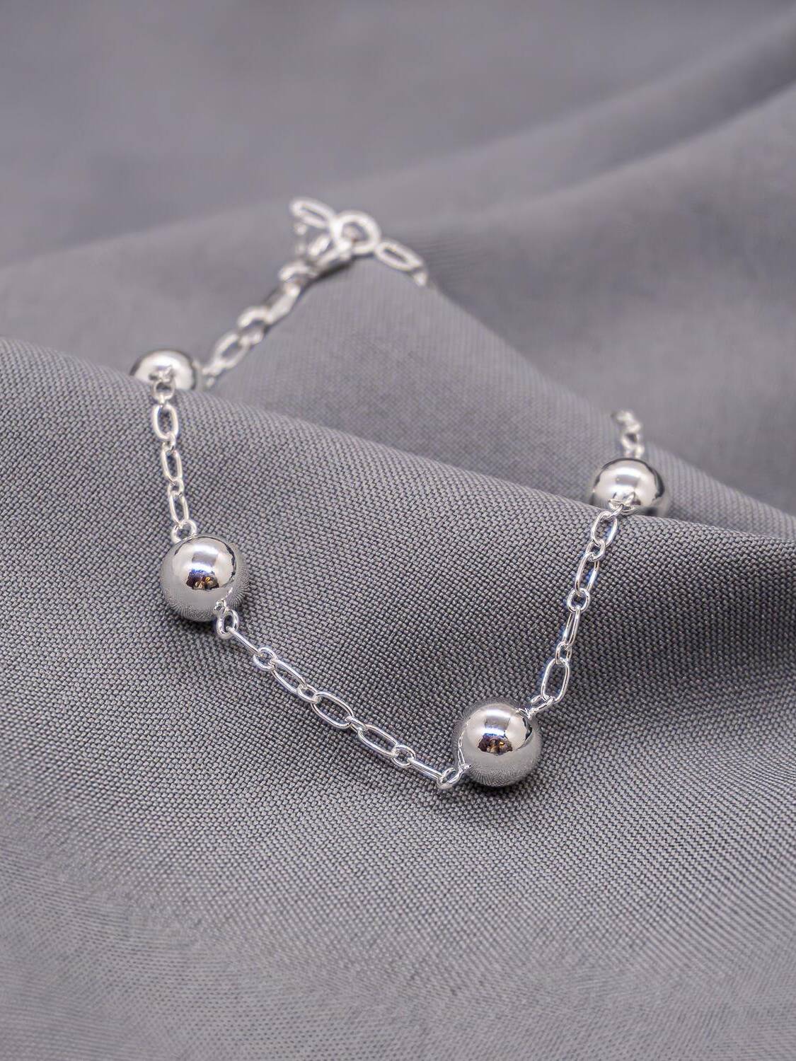 Bracelet argenté à chaîne de maillons allongés et boules lisses brillantes, sur tissu gris