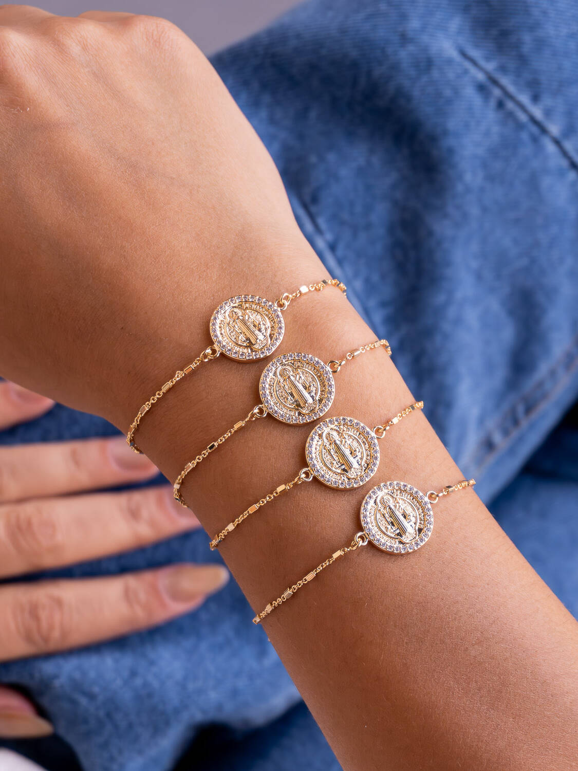 Poignet portant quatre bracelets dorés à médaille ronde de Saint Benoît bordée de pierres
