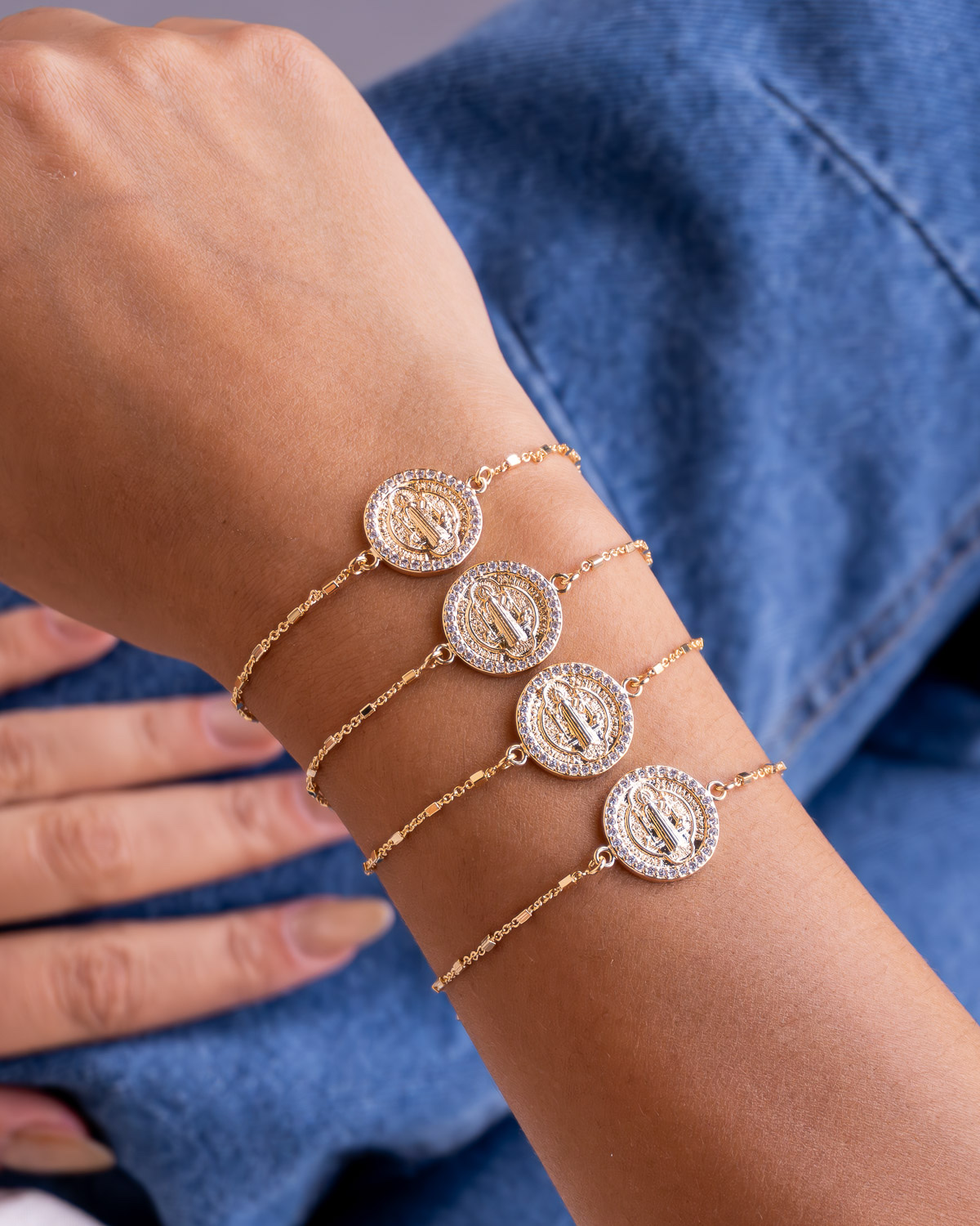 Poignet portant quatre bracelets dorés à médaille ronde de Saint Benoît bordée de pierres
