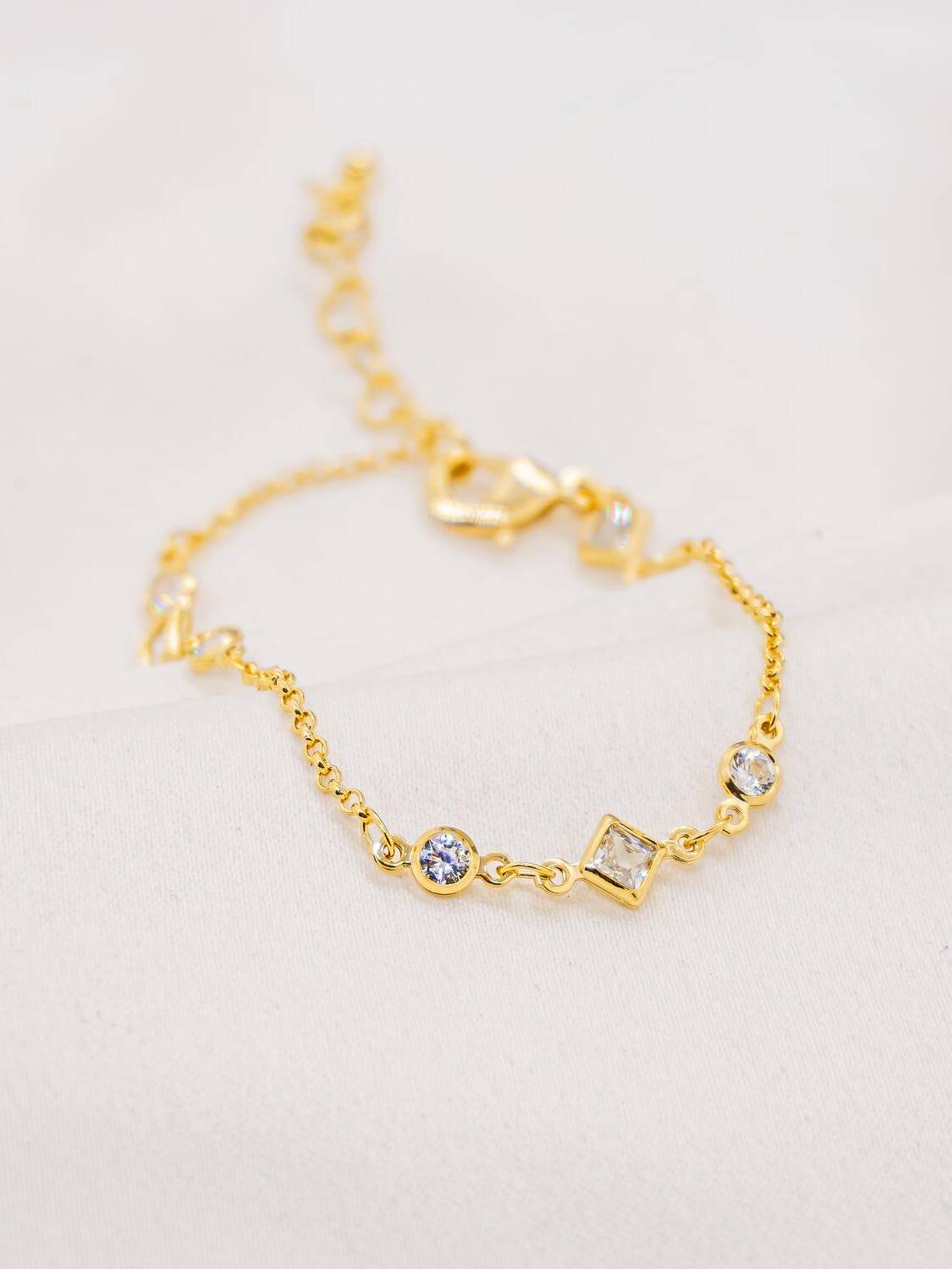 Bracelet doré en chaîne fine, pierres claires rondes et carrée serties, mousqueton et chaînette