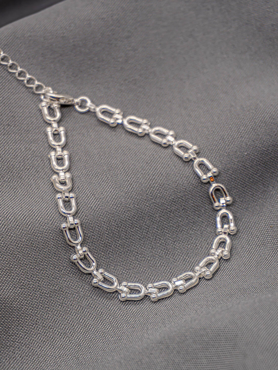 Bracelet argenté à maillons en U terminés par de petites boules, avec chaînette, sur tissu gris