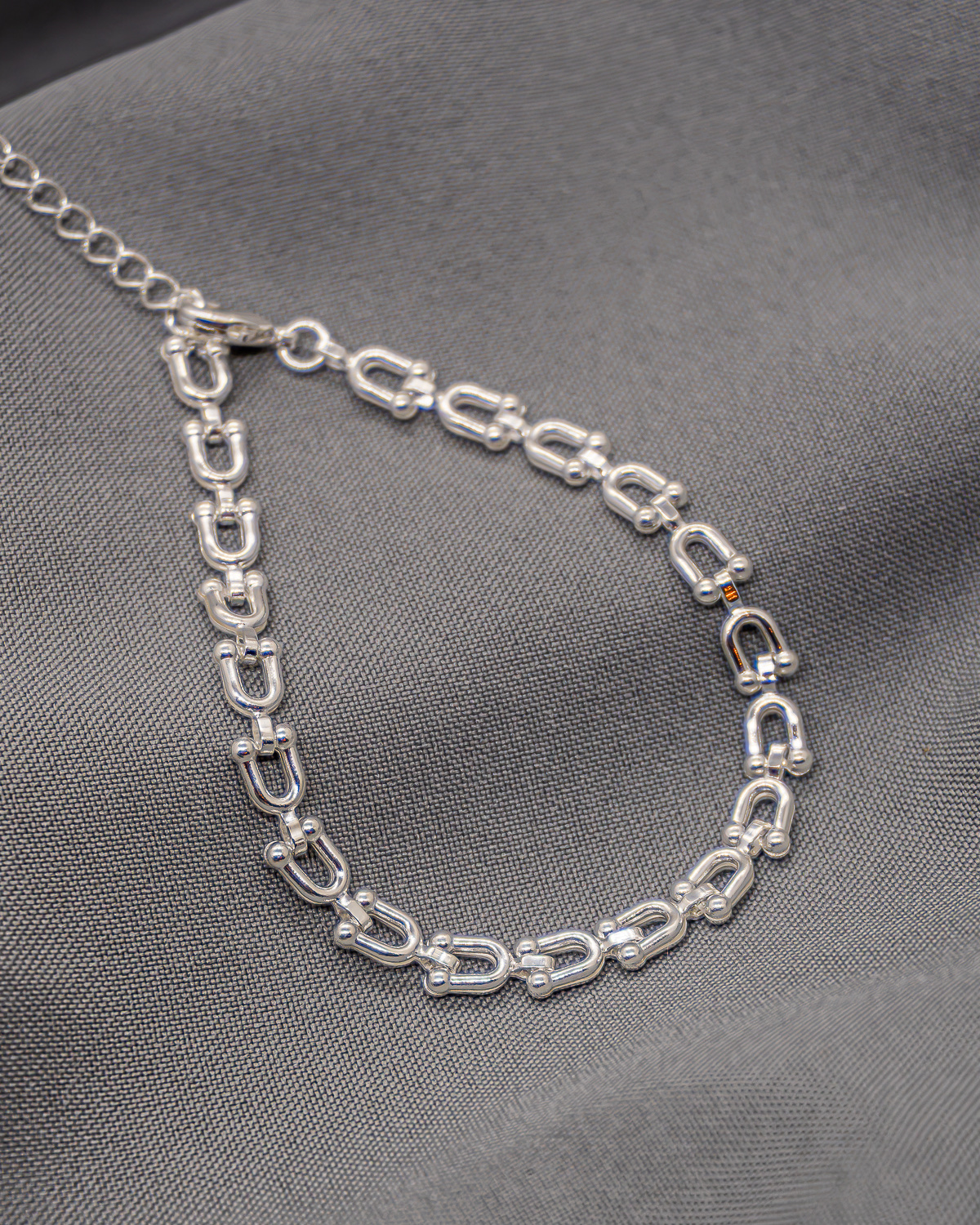 Bracelet argenté à maillons en U terminés par de petites boules, avec chaînette, sur tissu gris