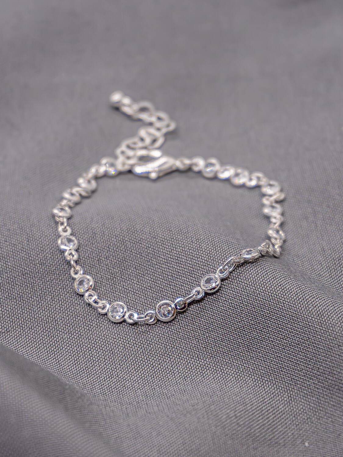 Bracelet argenté à petits maillons, pierres claires rondes serties, sur tissu gris