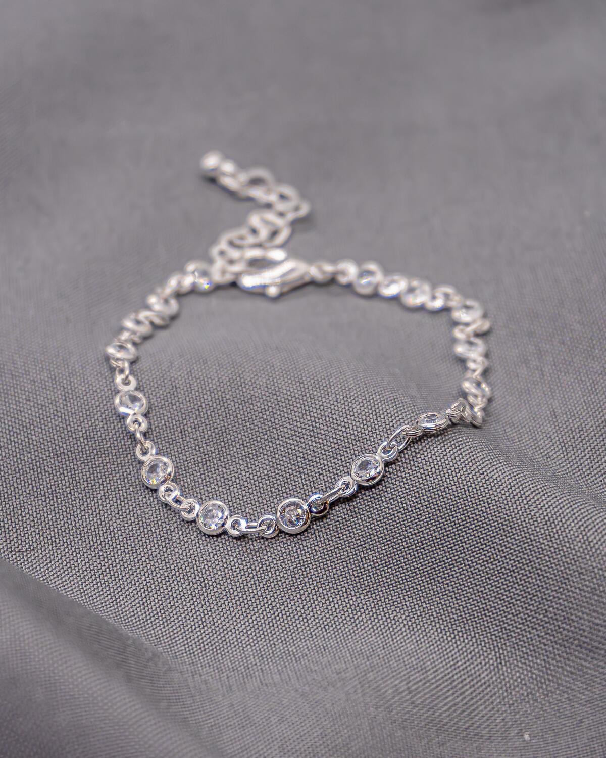 Bracelet argenté à petits maillons, pierres claires rondes serties, sur tissu gris