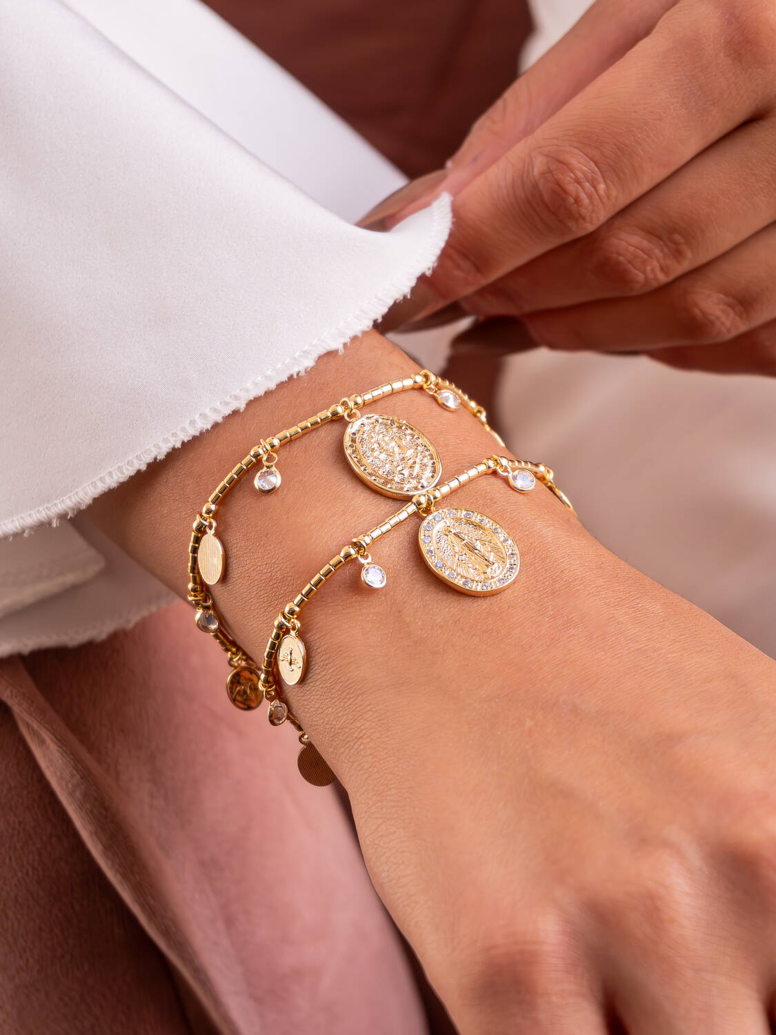 Deux bracelets dorés à perles tubes, grand médaillon ovale et petites médailles, portés au poignet