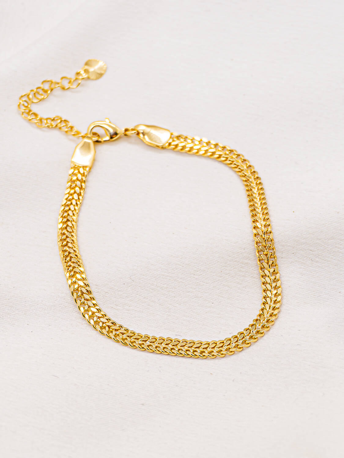 Bracelet doré à maille plate nattée en chevrons, avec mousqueton et chaînette d’extension, sur fond clair