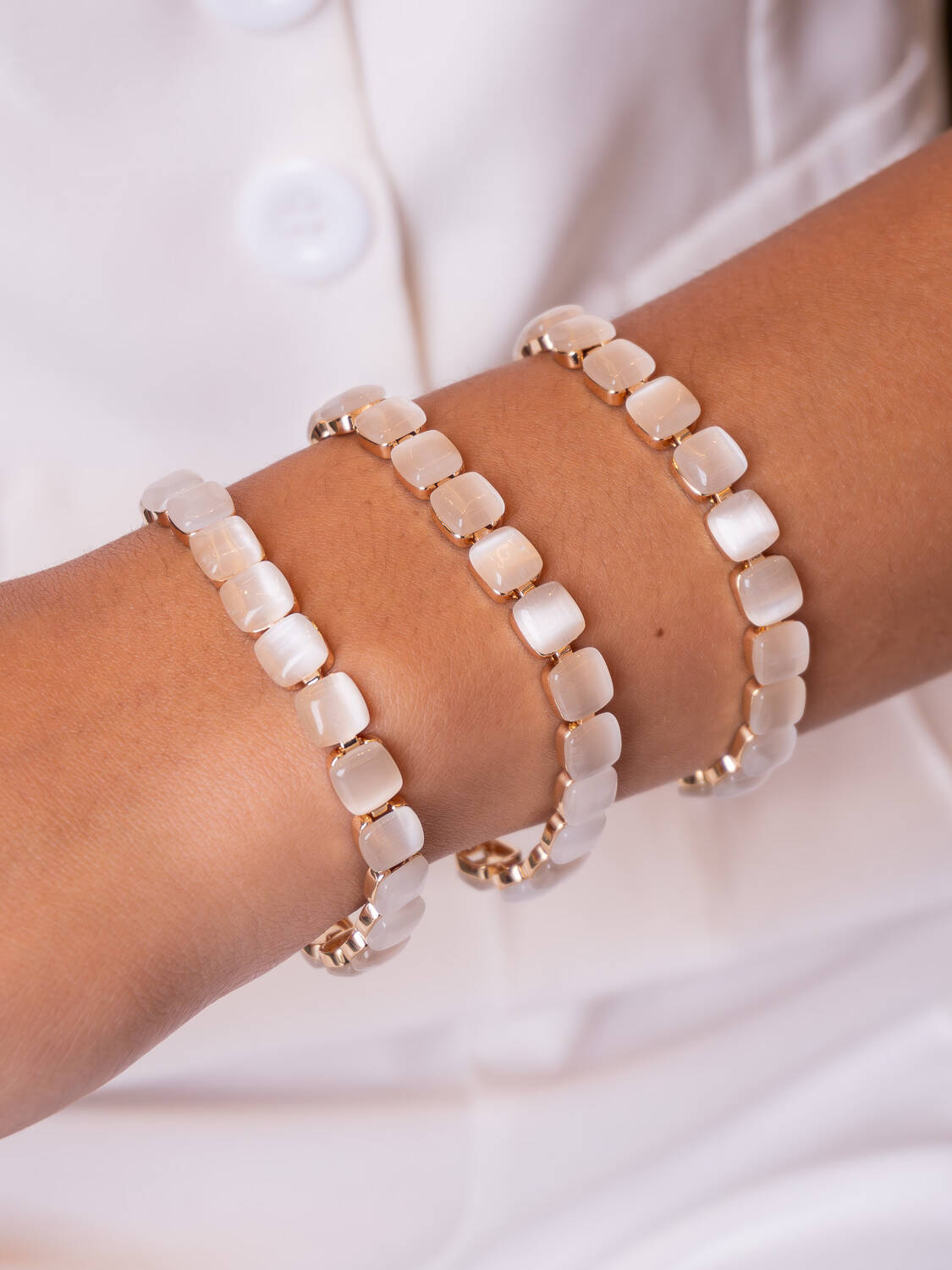 Trois bracelets de pierres carrées blanc laiteux montées dans un métal clair, portés sur un poignet