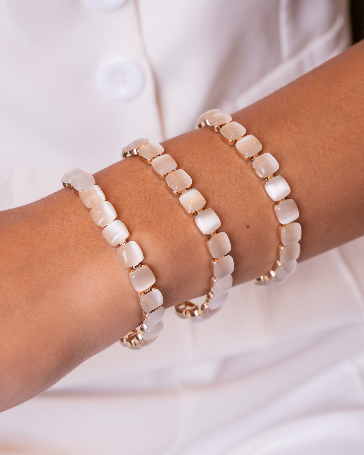 Trois bracelets de pierres carrées blanc laiteux montées dans un métal clair, portés sur un poignet