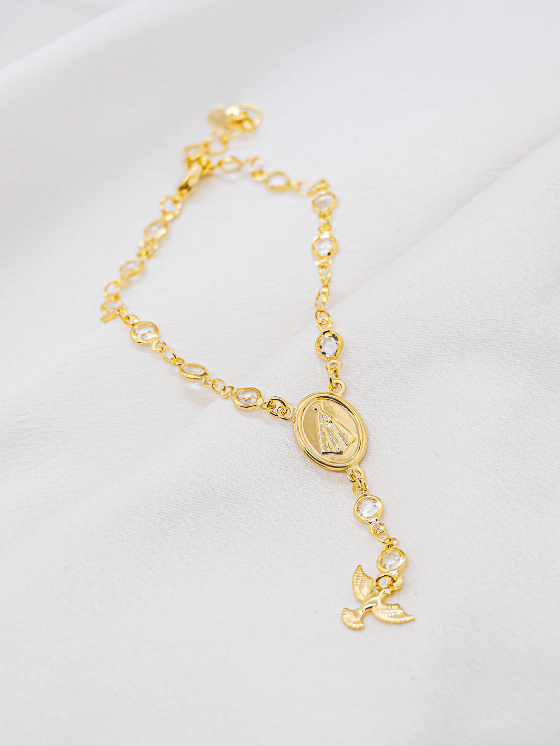 Bracelet doré à pierres claires serties, médaille ovale Notre-Dame et petite colombe pendante
