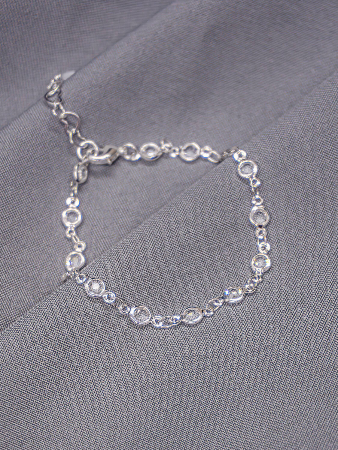 Bracelet argenté de petites pierres claires rondes serties, posé sur un tissu gris