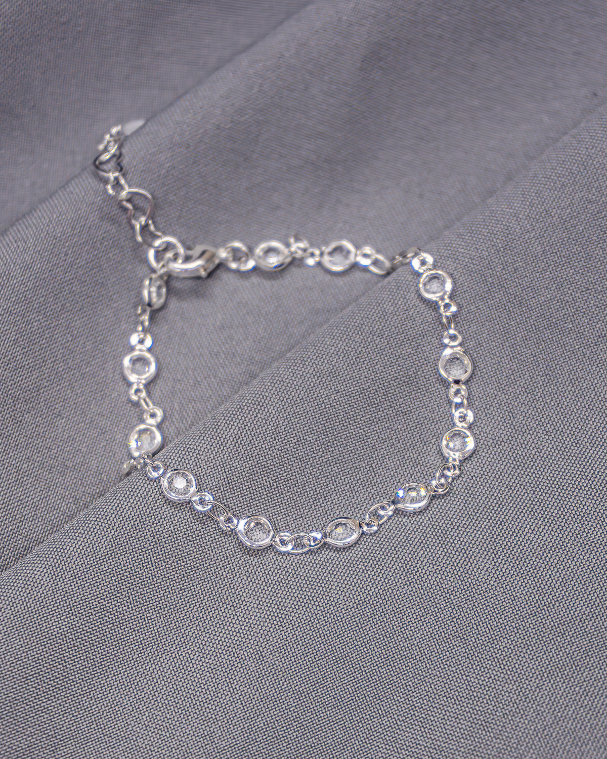 Silver bracelet with small round pavé-set clear stones, on grey fabric