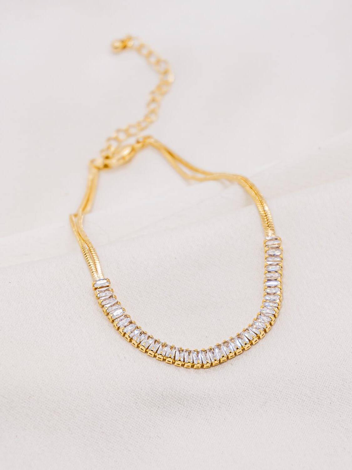 Bracelet doré à double chaîne fine et rivière de pierres claires taillées en baguette