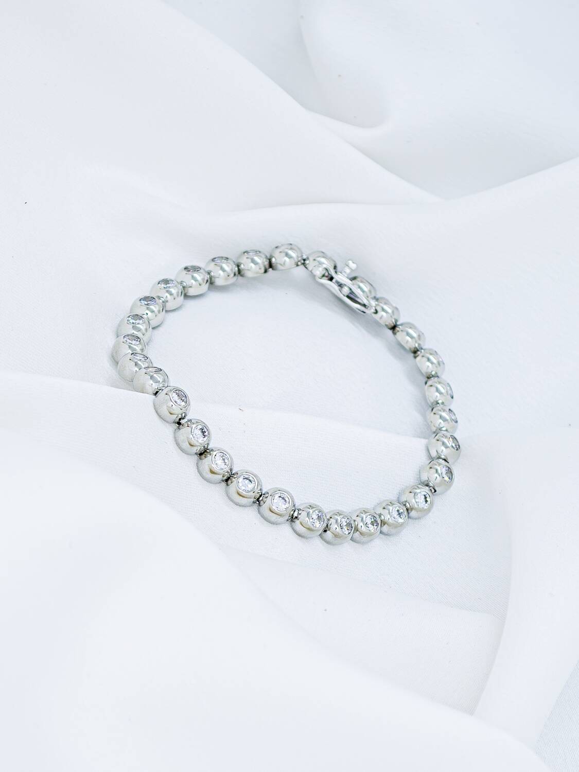 Bracelet rivière argenté composé de maillons bombés avec pierres claires serties, posé sur un tissu blanc