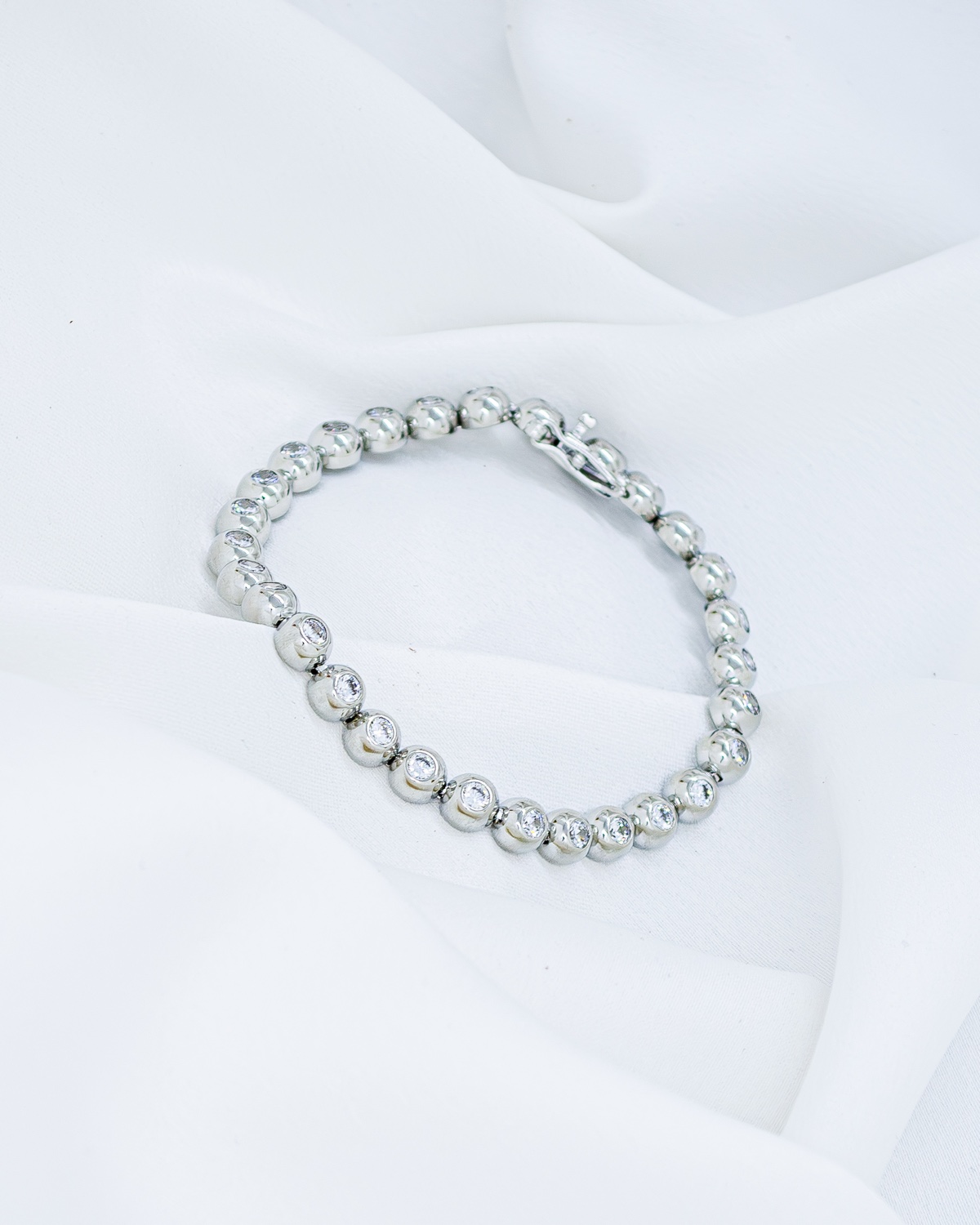 Bracelet rivière argenté composé de maillons bombés avec pierres claires serties, posé sur un tissu blanc
