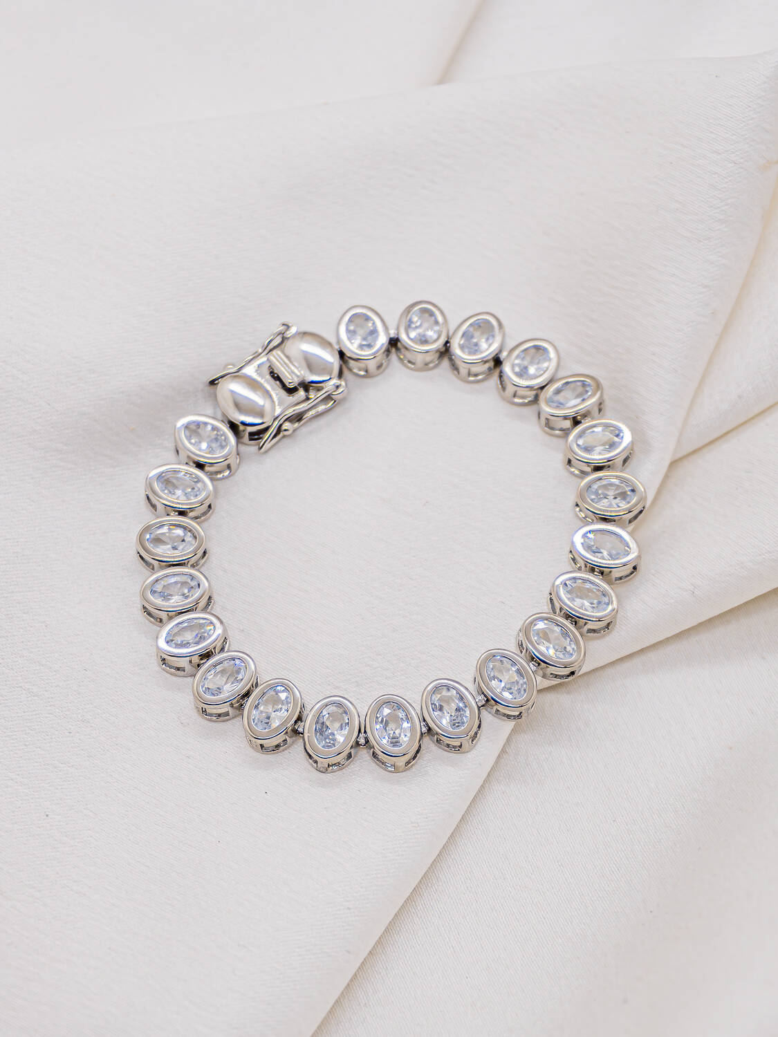 Bracelet rivière argenté de pierres claires ovales serties, avec fermoir plat, sur tissu crème
