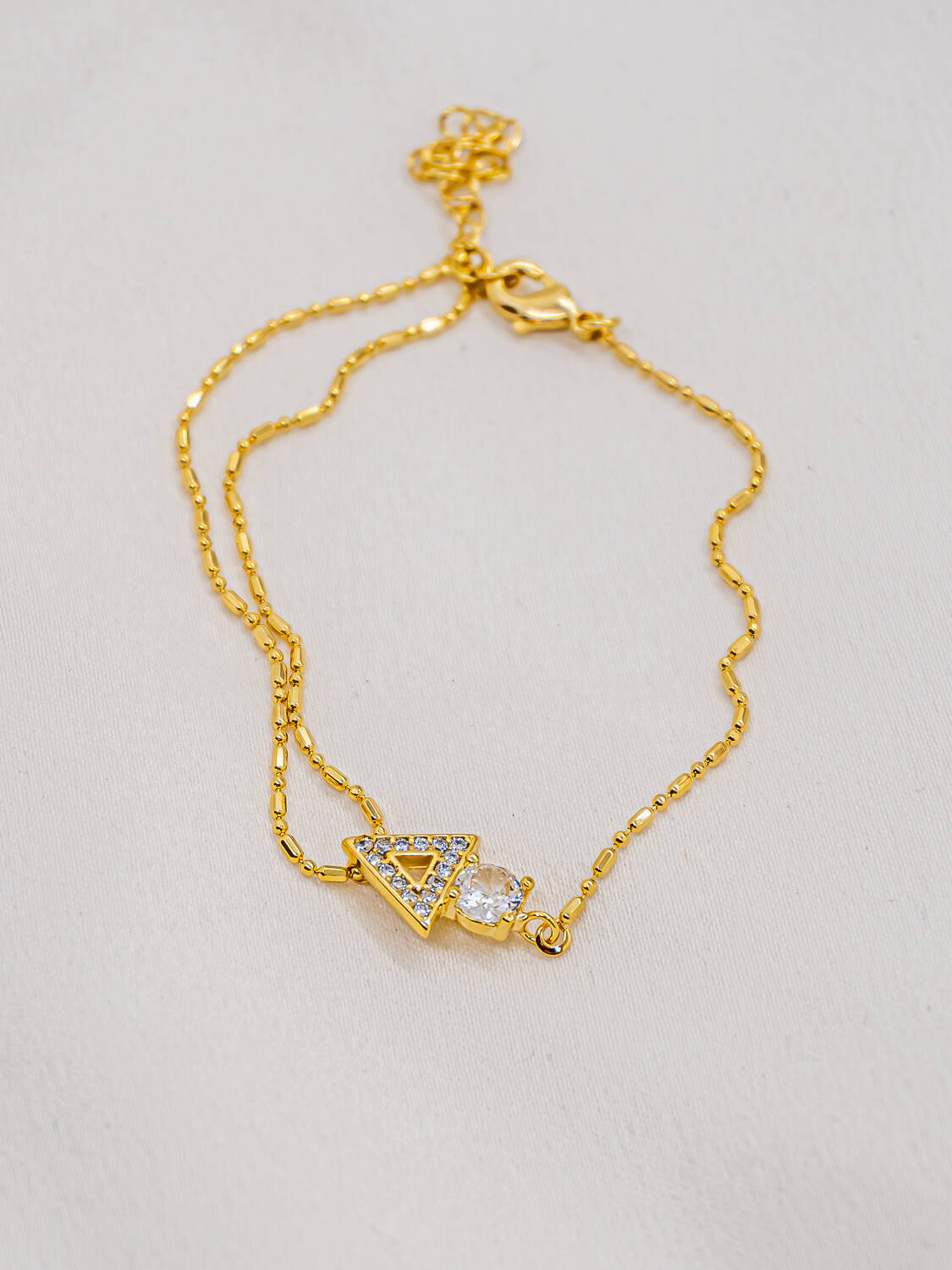 Bracelet doré à deux chaînes fines avec triangle serti et grande pierre claire ronde