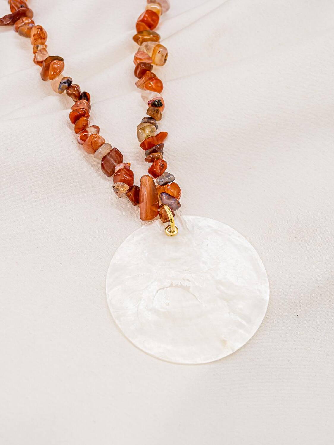 Collier de petits éclats d’agate orangés avec grand disque de nacre blanche, sur tissu clair