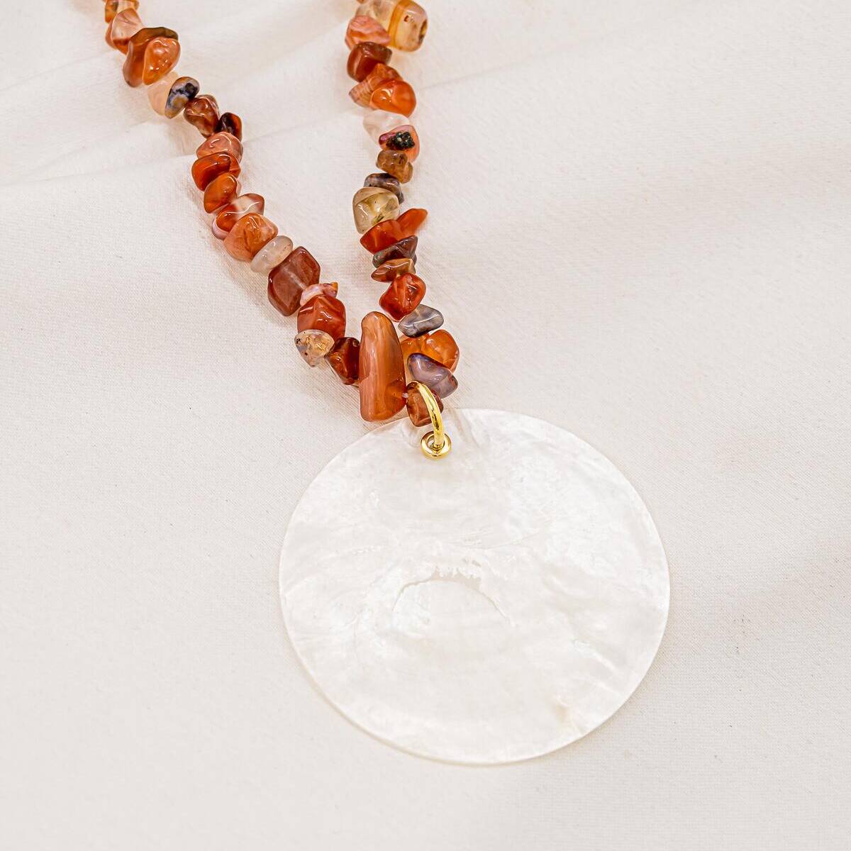 Orange agate chip necklace with large white mother-of-pearl disc, on light fabric
