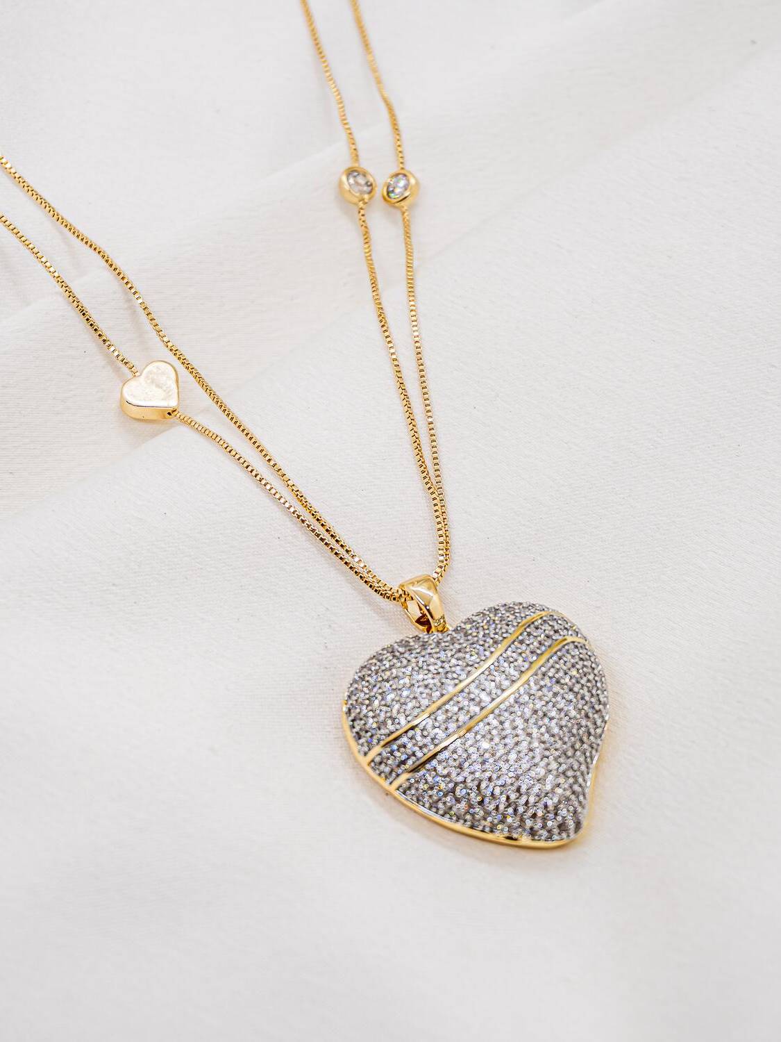 Collier à deux fines chaînes, petit cœur lisse et grand cœur serti de pierres claires