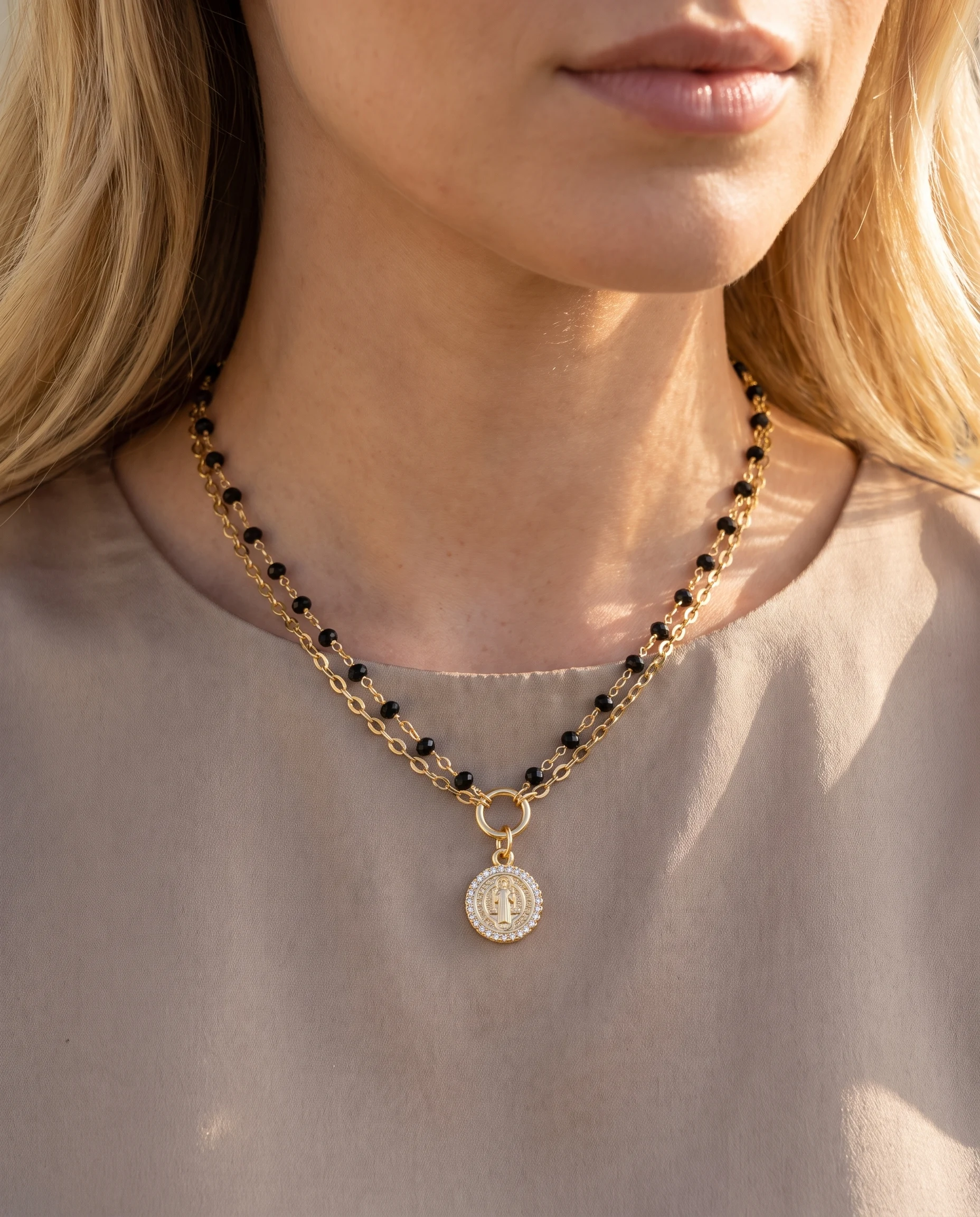 Collier doré double rang à cristaux noirs et petite médaille de saint Benoît, porté au cou, vu de près