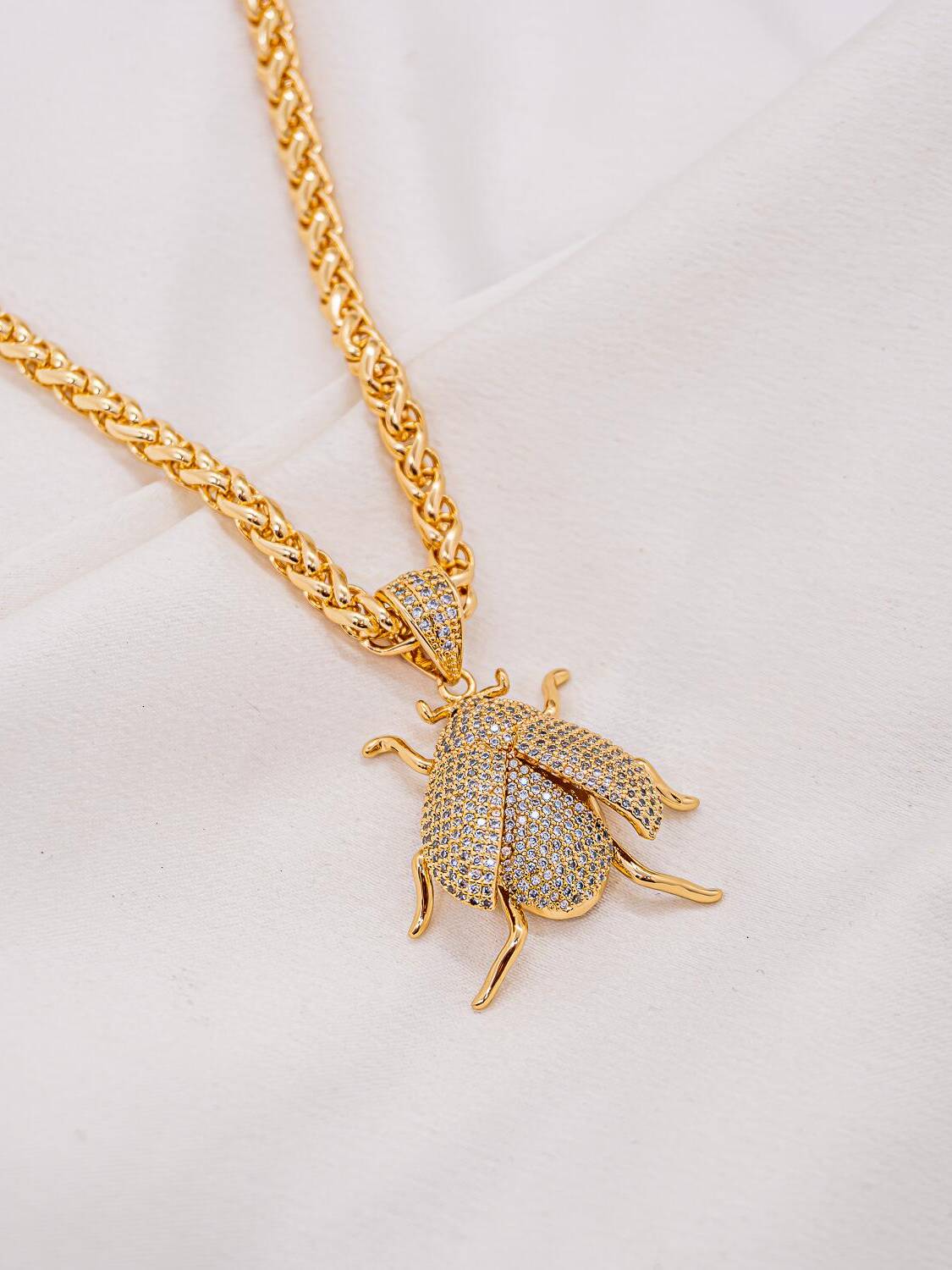 Collier doré à chaîne épaisse entrelacée et pendentif scarabée aux ailes serties de pierres claires