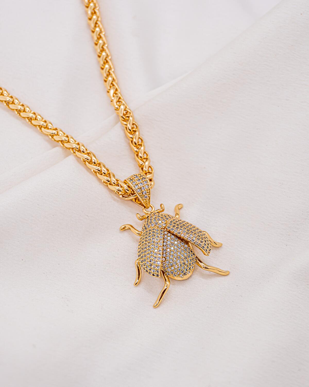 Collier doré à chaîne épaisse entrelacée et pendentif scarabée aux ailes serties de pierres claires
