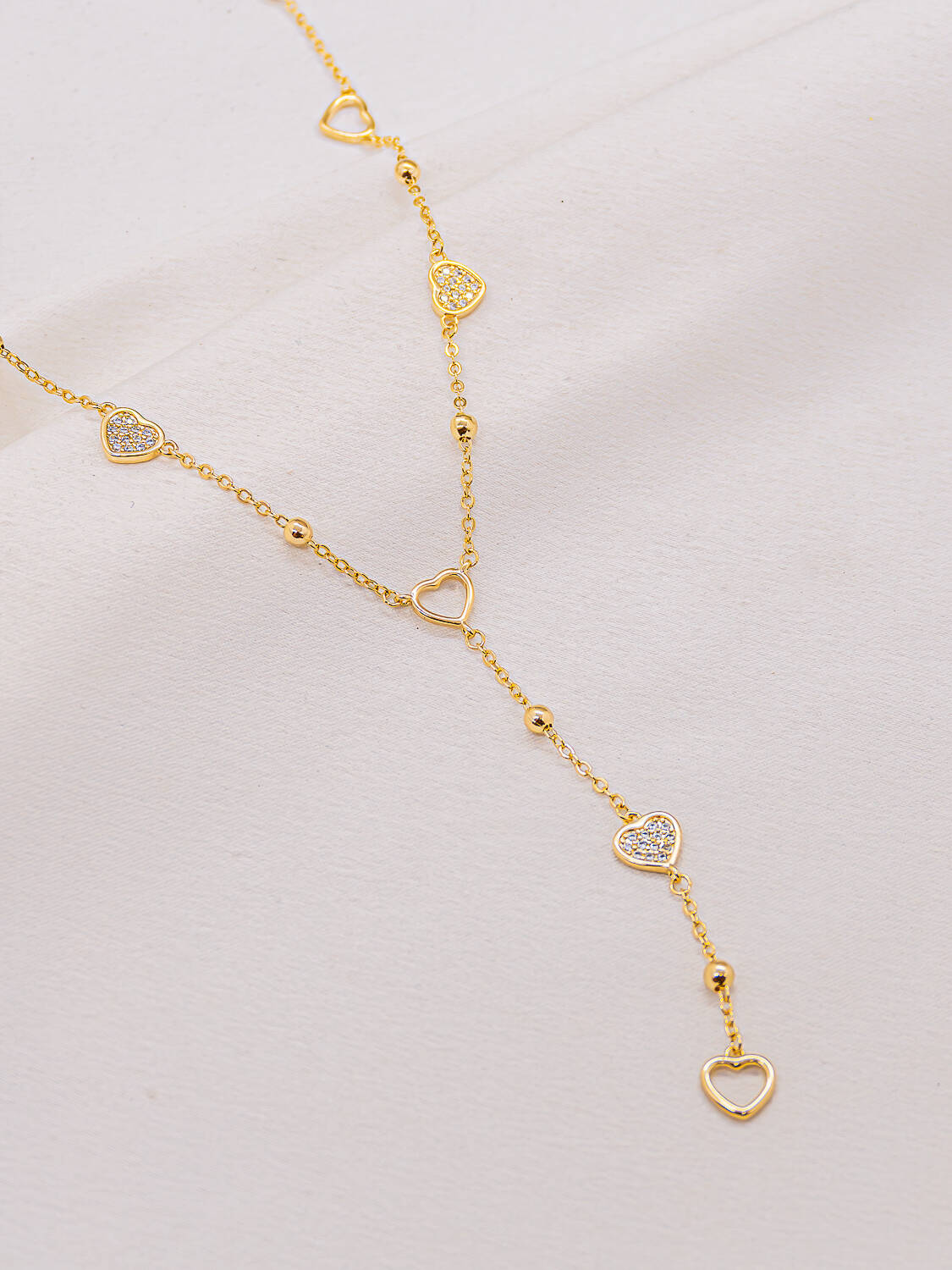 Collier doré forme cravate à cœurs ajourés et cœurs sertis, posé sur un tissu clair