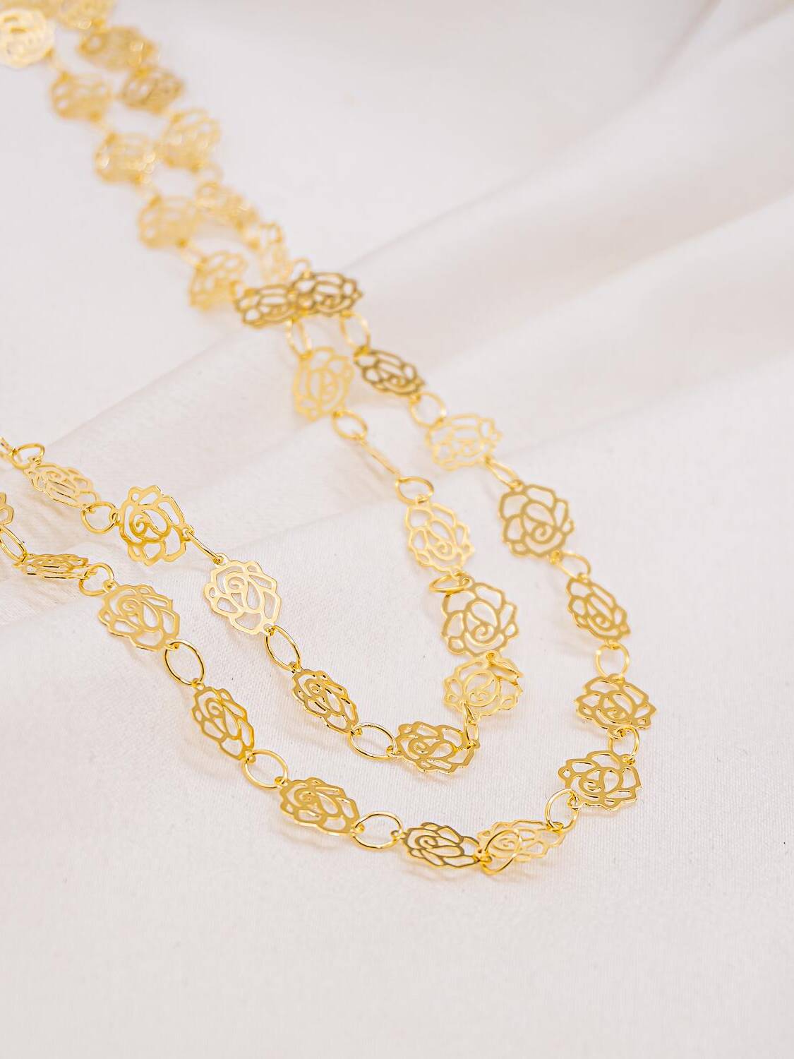 Long collier doré de fleurs ajourées lisses reliées par des anneaux ovales, porté en deux rangs