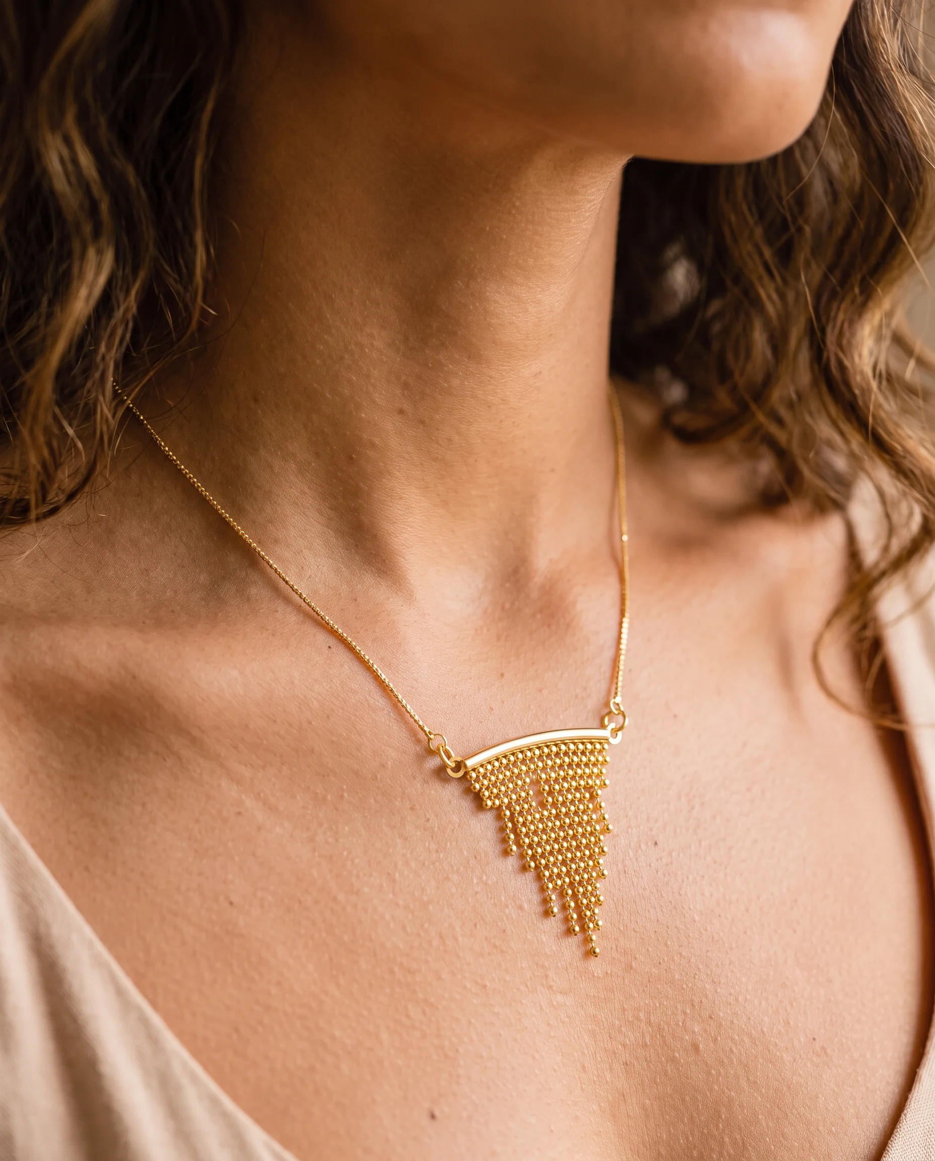 Collier doré fin à frange triangulaire de minuscules billes, porté sur la poitrine, vu de près