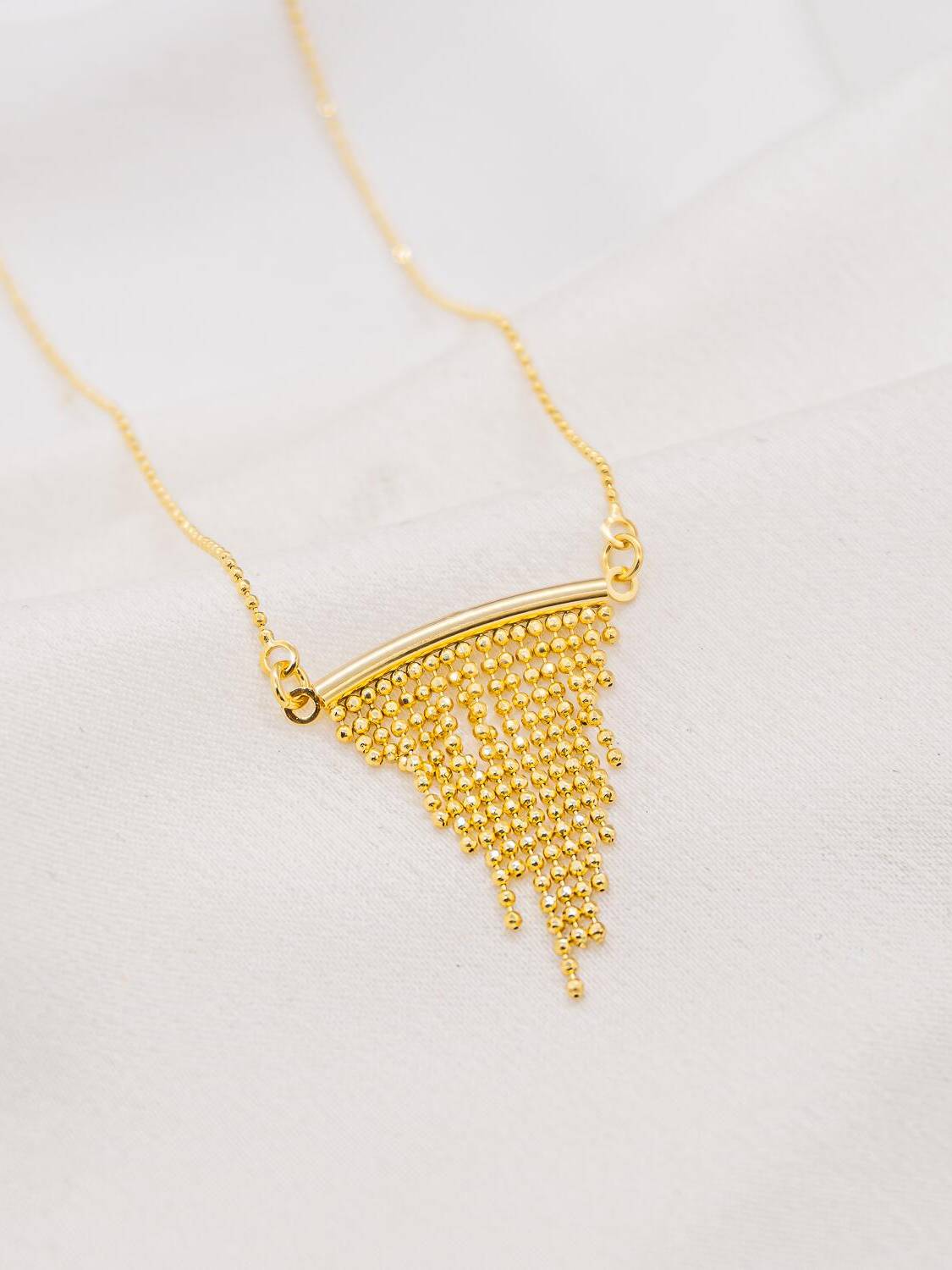 Collier doré, barrette courbe d’où tombent des franges de minuscules billes, sur chaîne fine