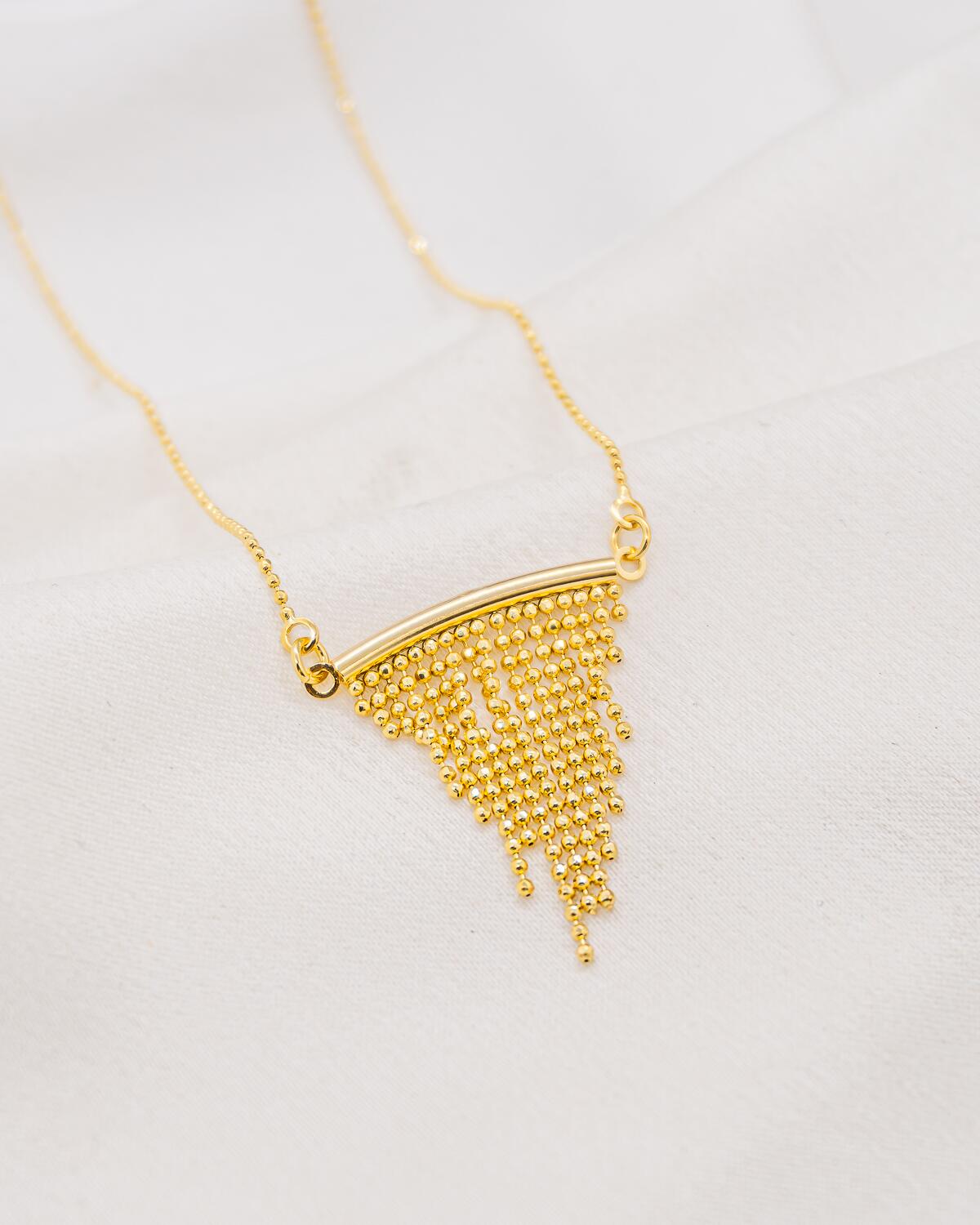 Collier doré, barrette courbe d’où tombent des franges de minuscules billes, sur chaîne fine