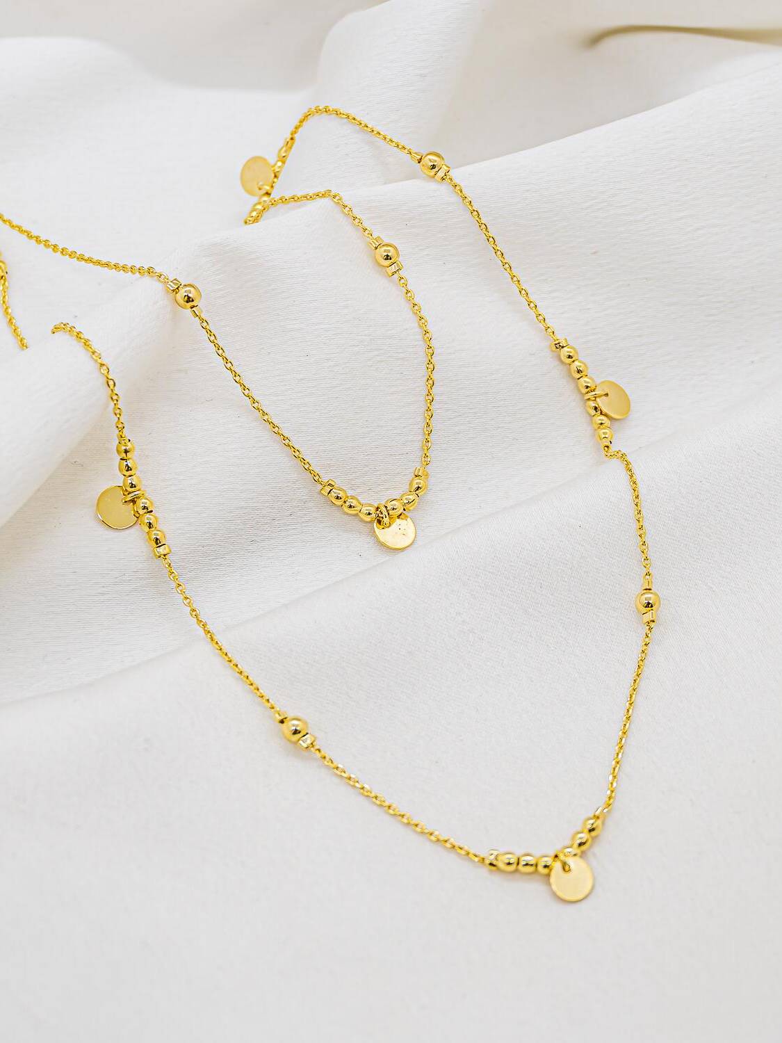Collier long doré, fine chaîne, petites boules lisses et petites médailles rondes, sur tissu