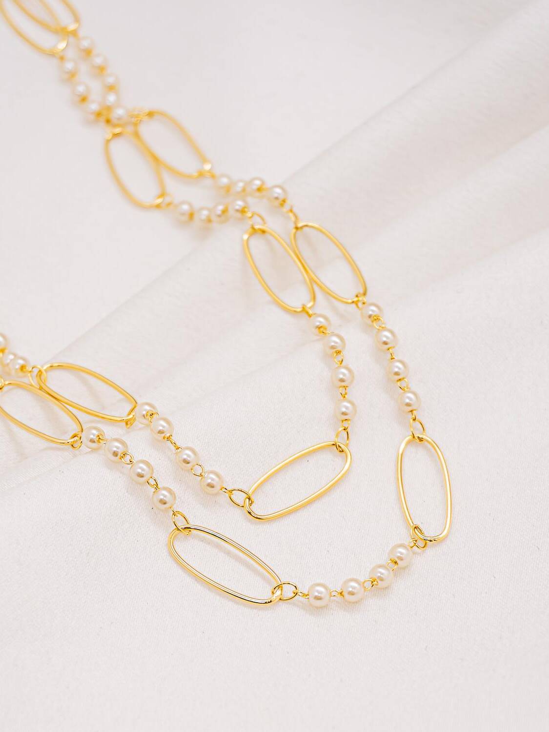 Long collier doré alternant petites perles ivoire et grands maillons ovales, porté en deux rangs