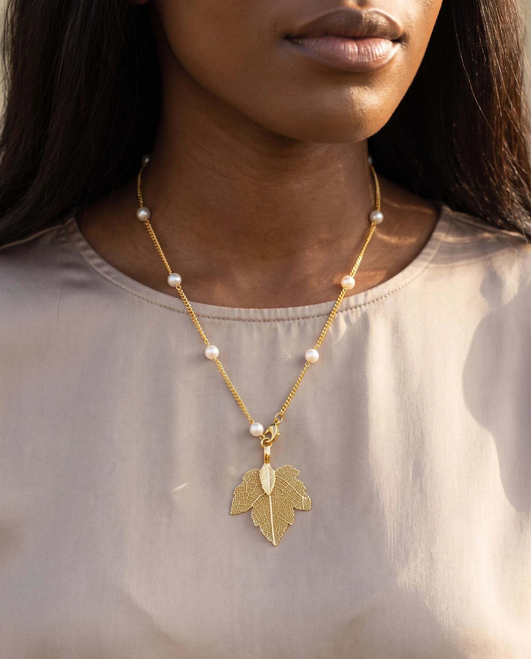 Long collier doré à perles blanches et pendentif feuille ajourée, porté en sautoir, vu de près