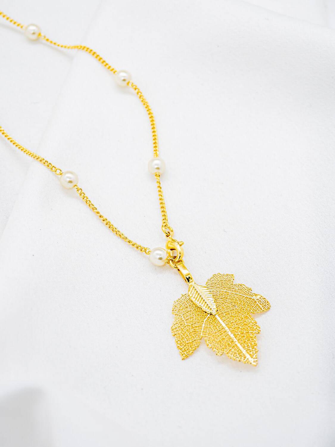 Collier long doré avec petites perles blanches rondes et pendentif feuille dorée ajourée